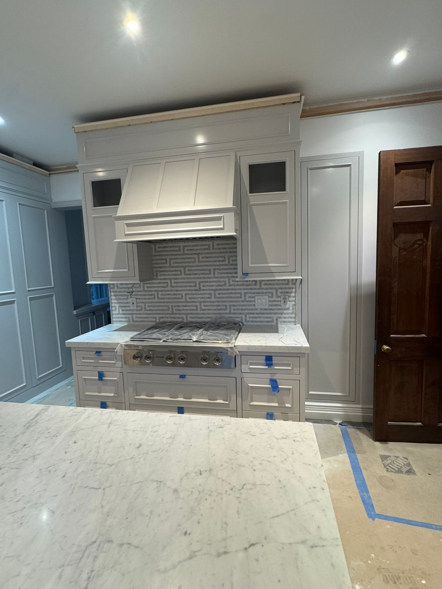 Modern white kitchen with stainless range, tiled backsplash, and marble island countertop