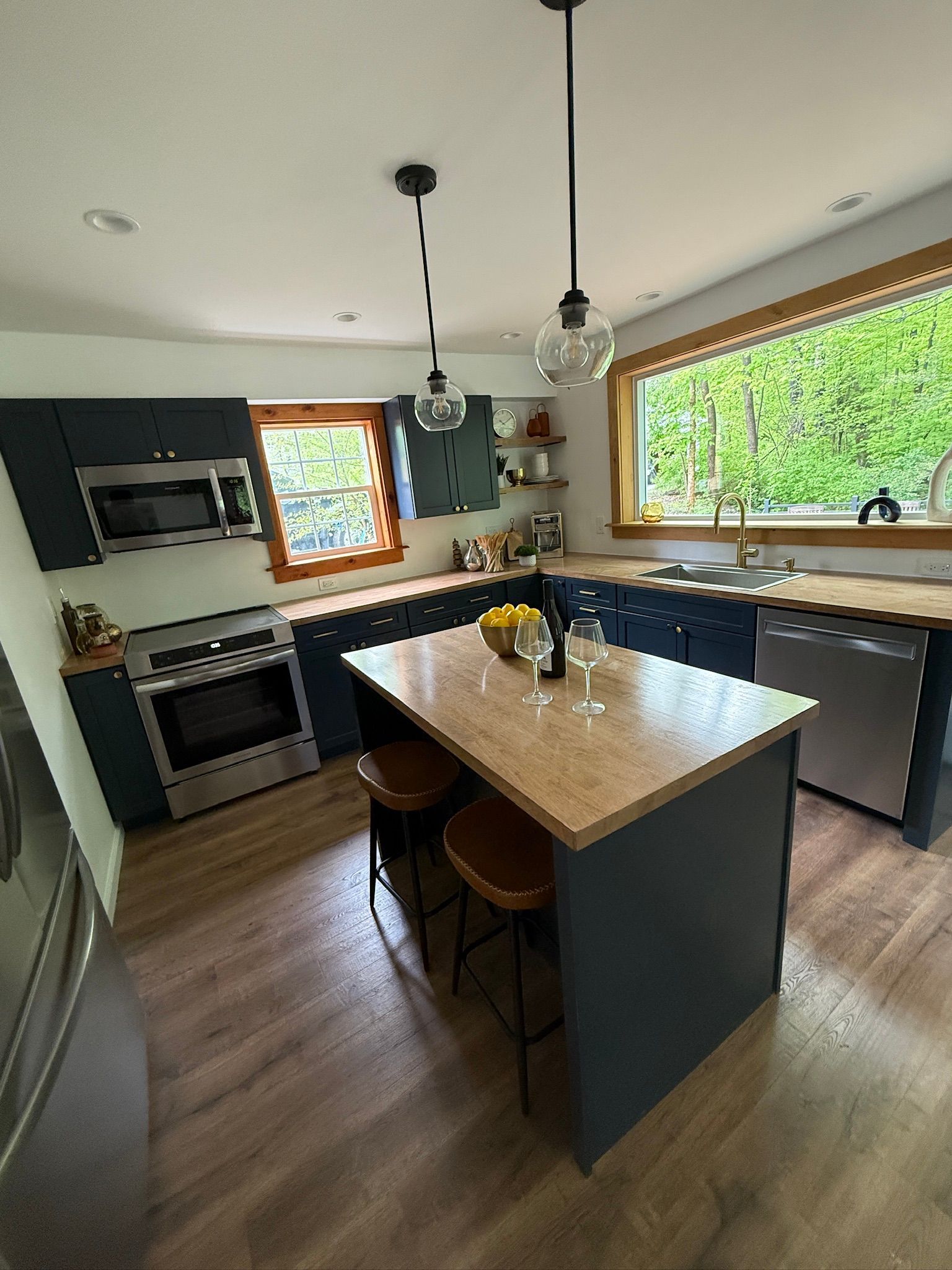 Modern kitchen with dark cabinets, wood island, pendant lights, and large window over the sink