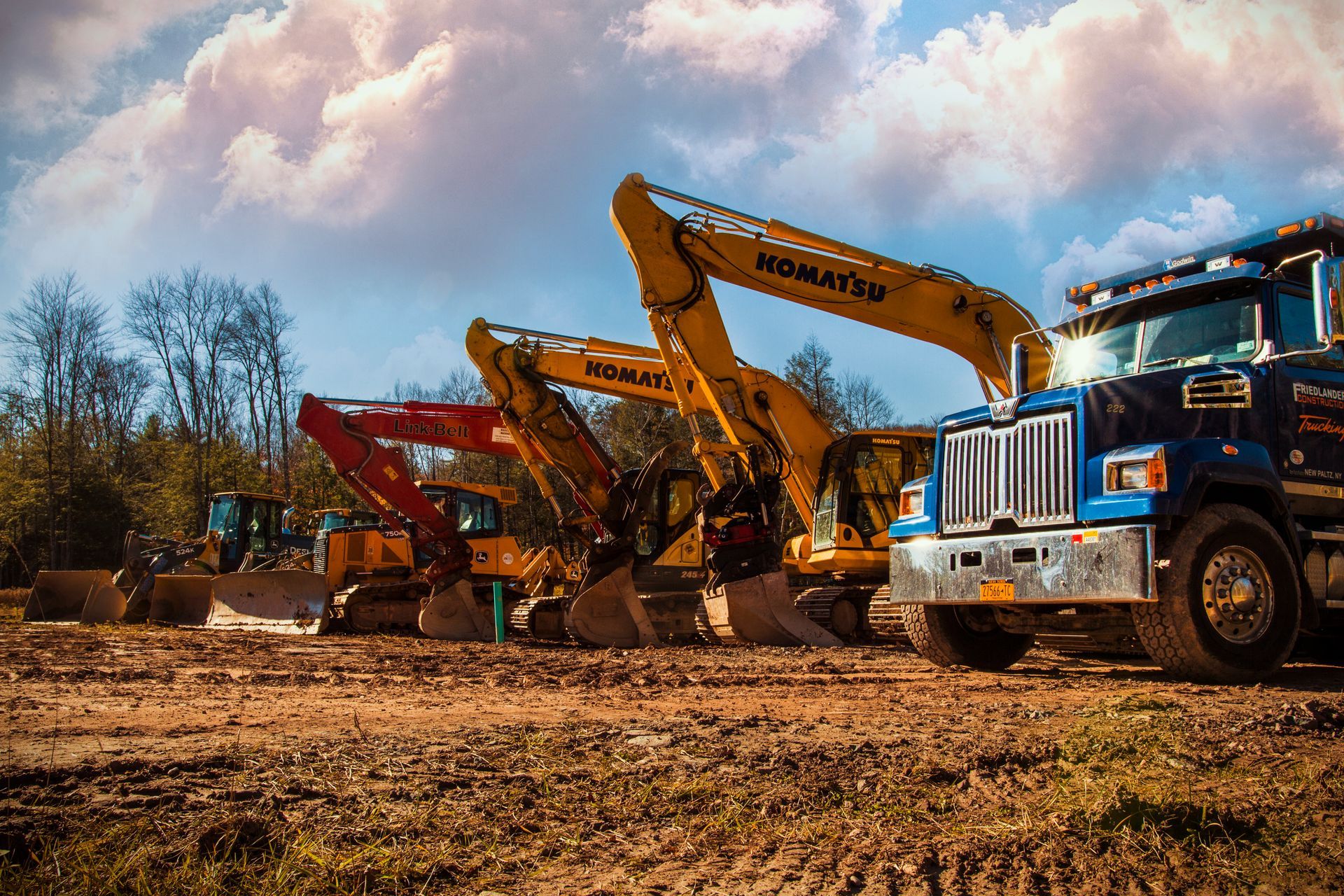 Excavators and a dump truck working on a dirt construction site under a cloudy sky