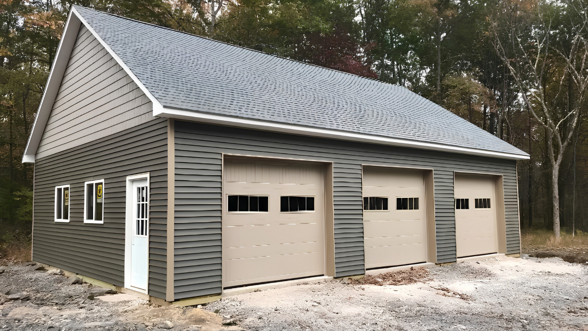 Three-car detached garage with gray siding and beige doors in a wooded setting