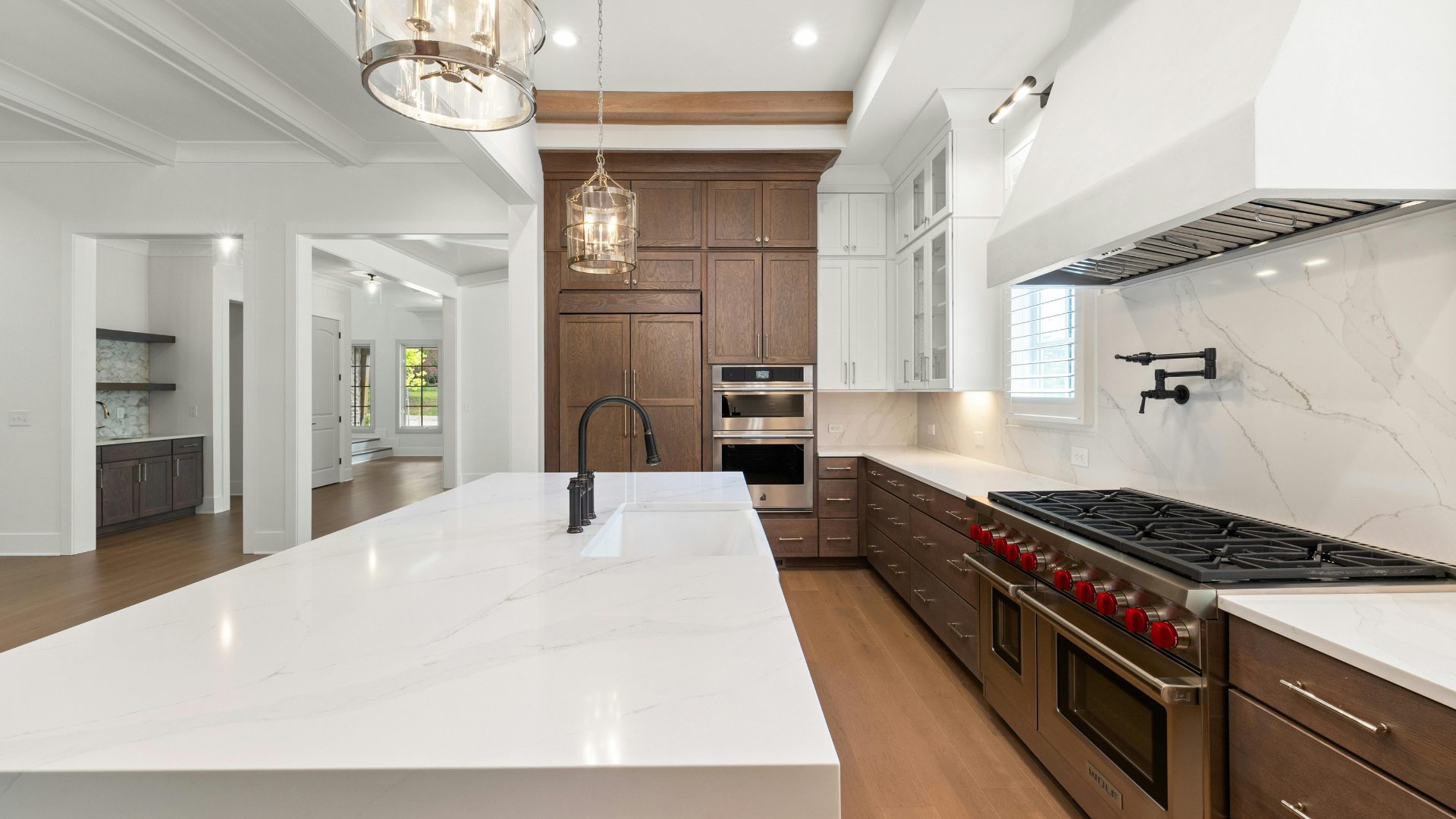Bright modern kitchen with white island, marble counters, wood floors, and stainless steel appliances