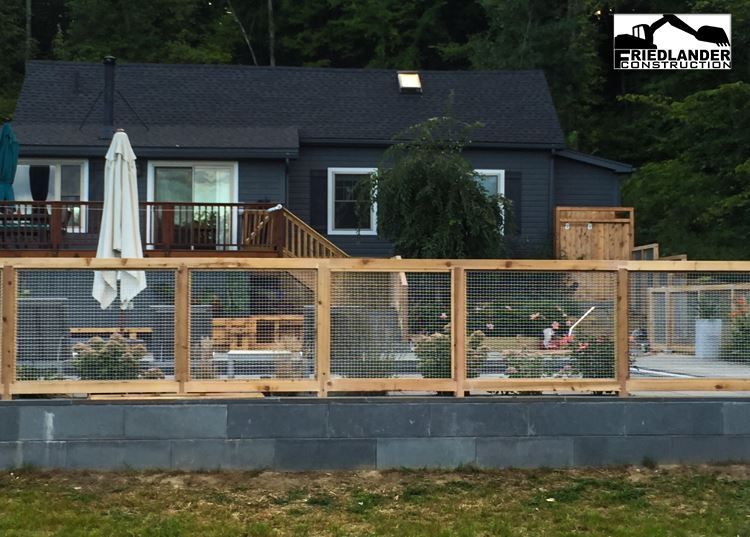 Nighttime view of a modern house with a wooden deck, fenced yard, and patio umbrella under lights