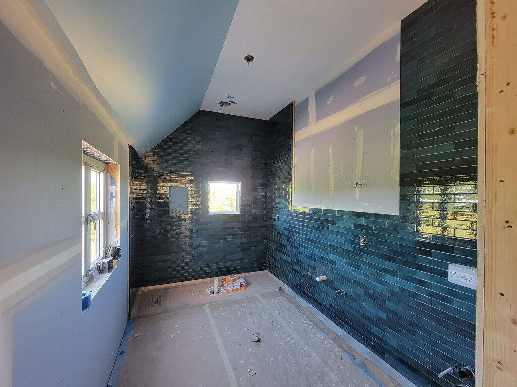 Narrow bathroom under renovation with dark blue tiled walls, white ceiling, and unfinished floor