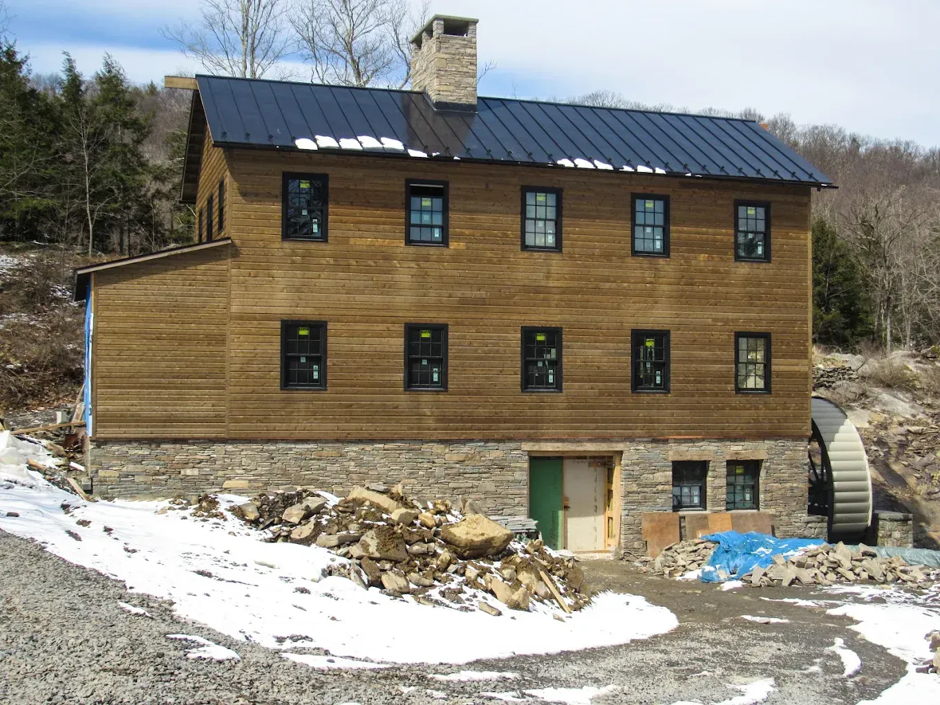 Wood-sided house on a snowy hillside with a dark roof and stone chimney