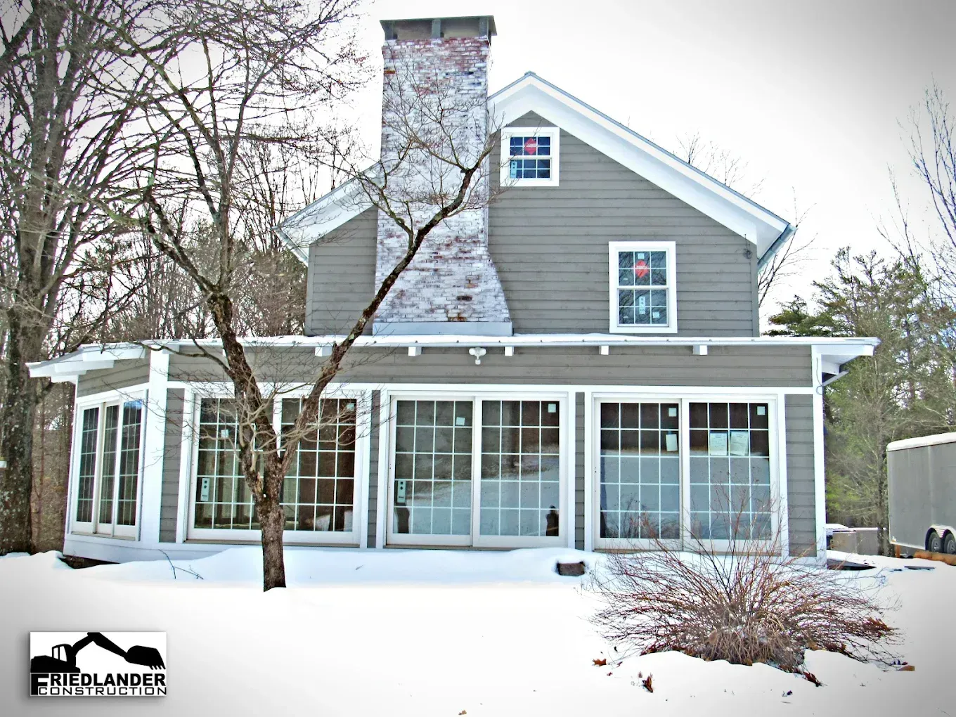 Snow-covered gray house with a stone chimney and screened porch in winter