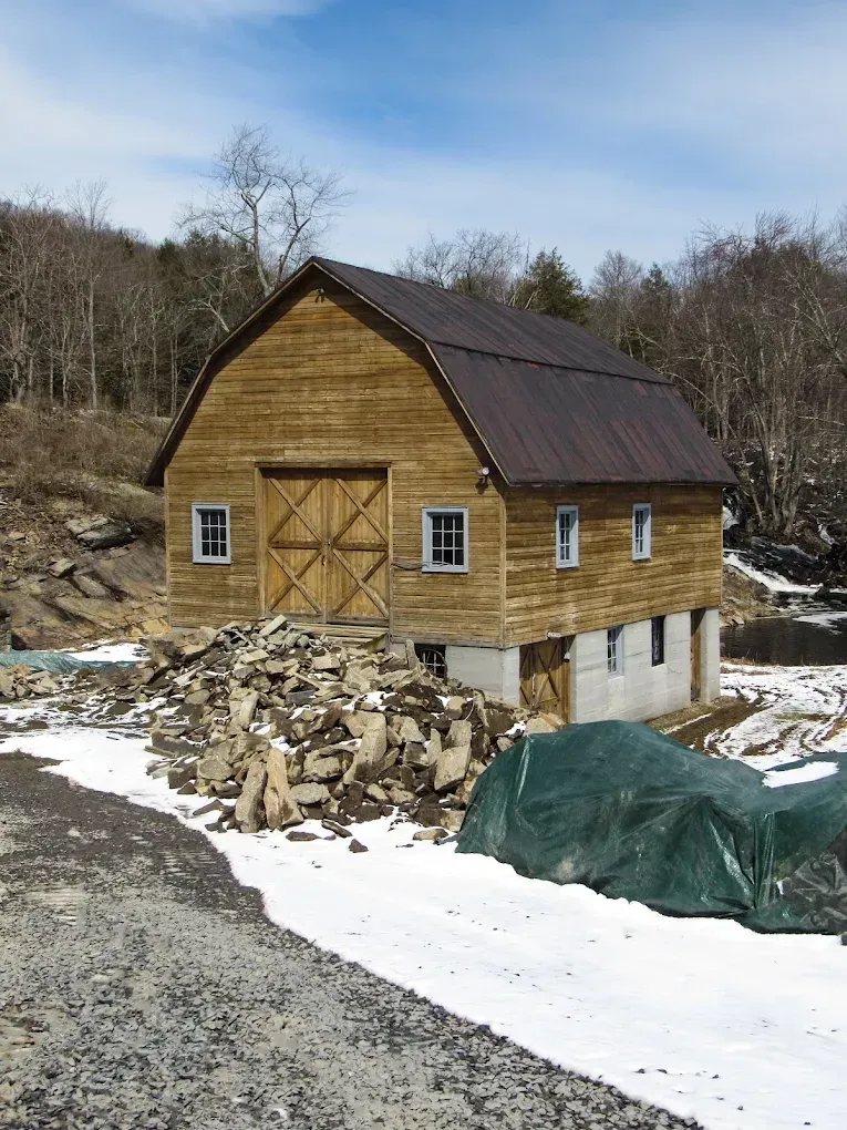 Small wooden barn under construction with snow on the ground and building materials piled nearby