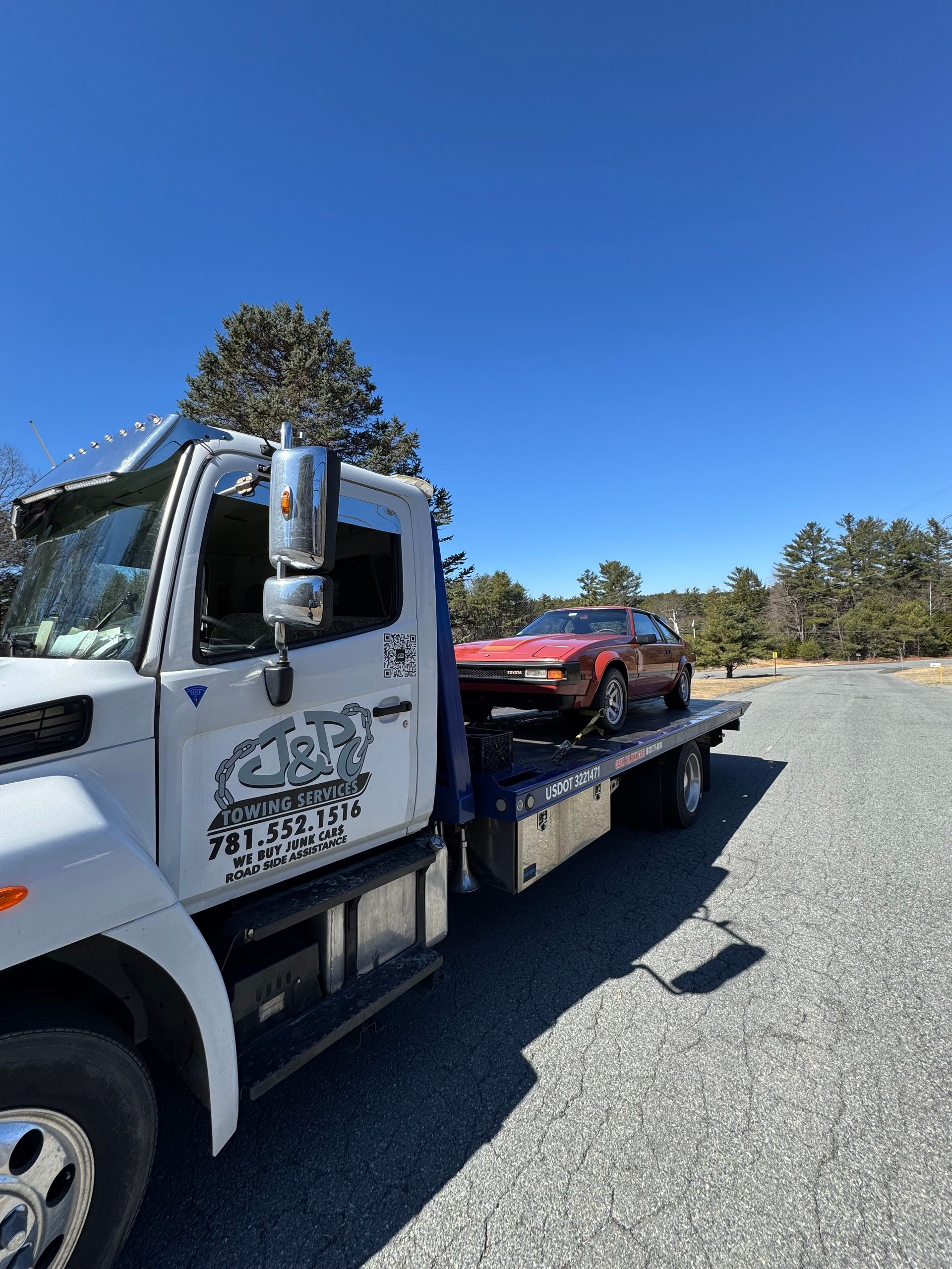 A tow truck is towing a red car in a parking lot.