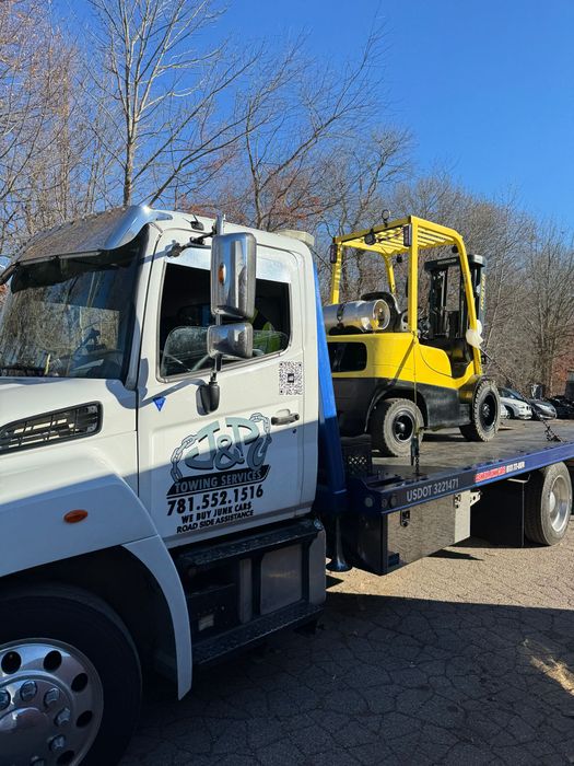 A yellow forklift is sitting on the back of a tow truck.