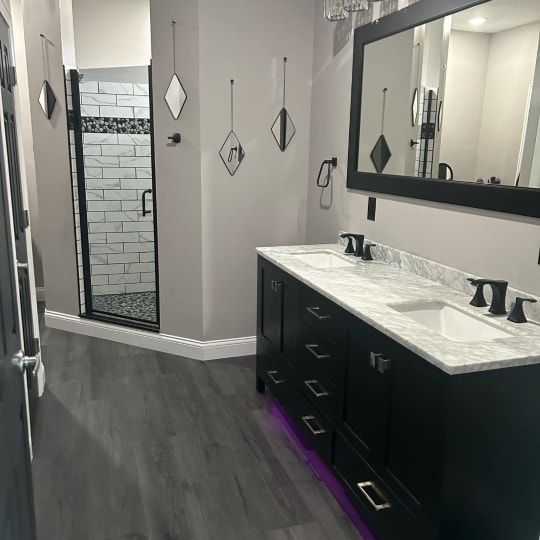 Modern bathroom with double vanity, black cabinets, marble countertop, and glass shower door
