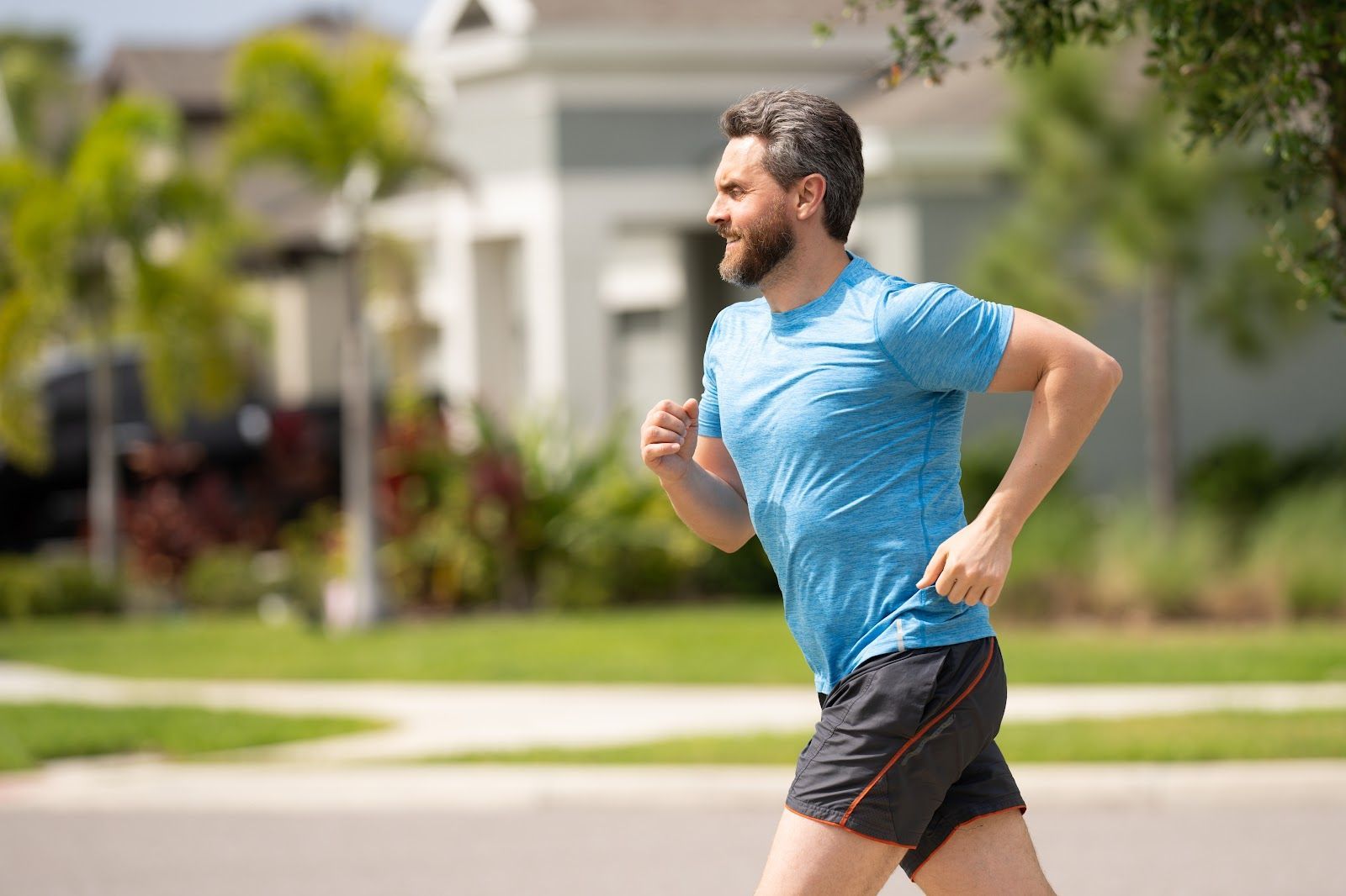 Man in blue shirt and black shorts running outdoors, smiling.