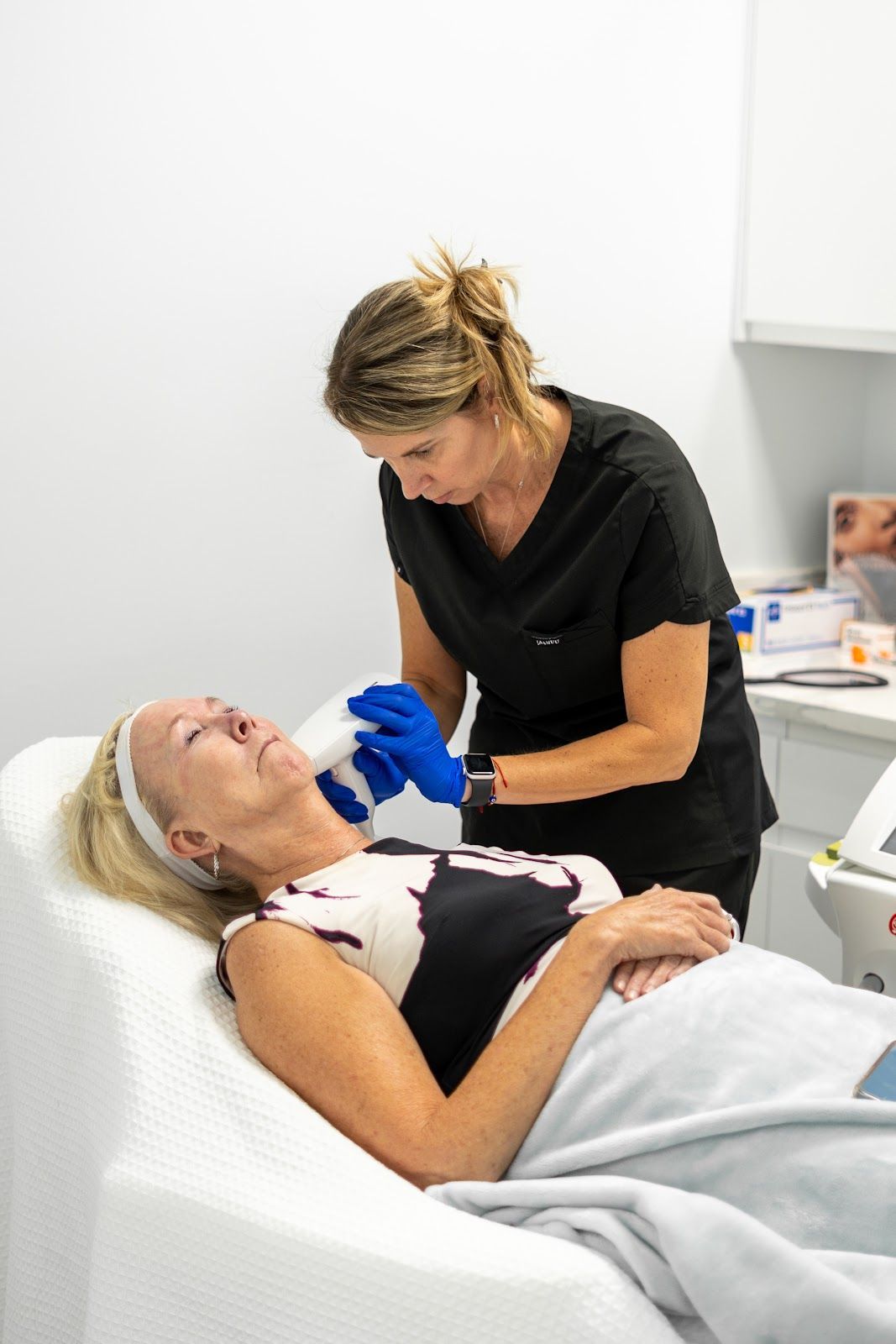 Woman receiving cosmetic treatment on her face from a medical professional. White clinic room.