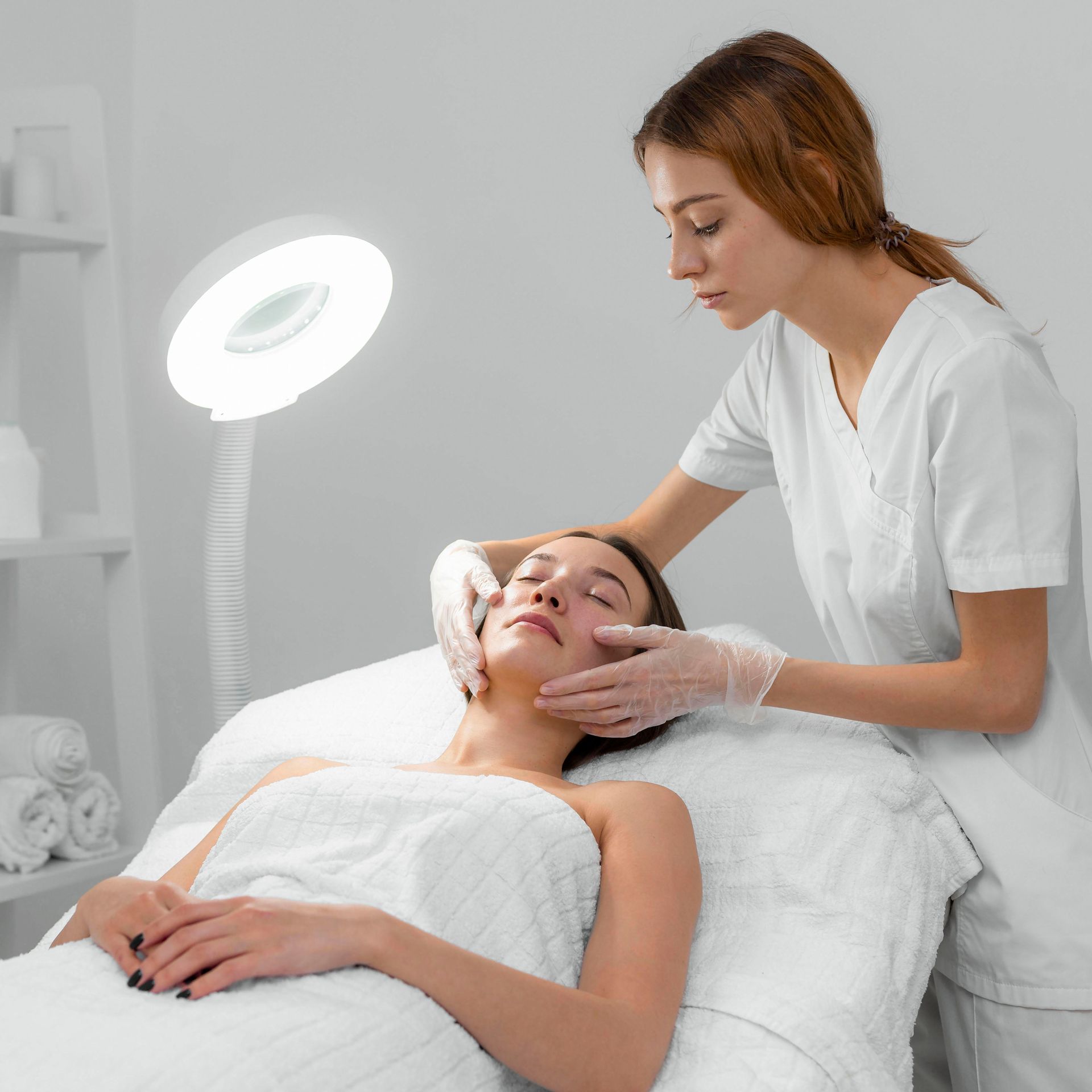 A woman is laying on a bed getting a facial treatment from a nurse.