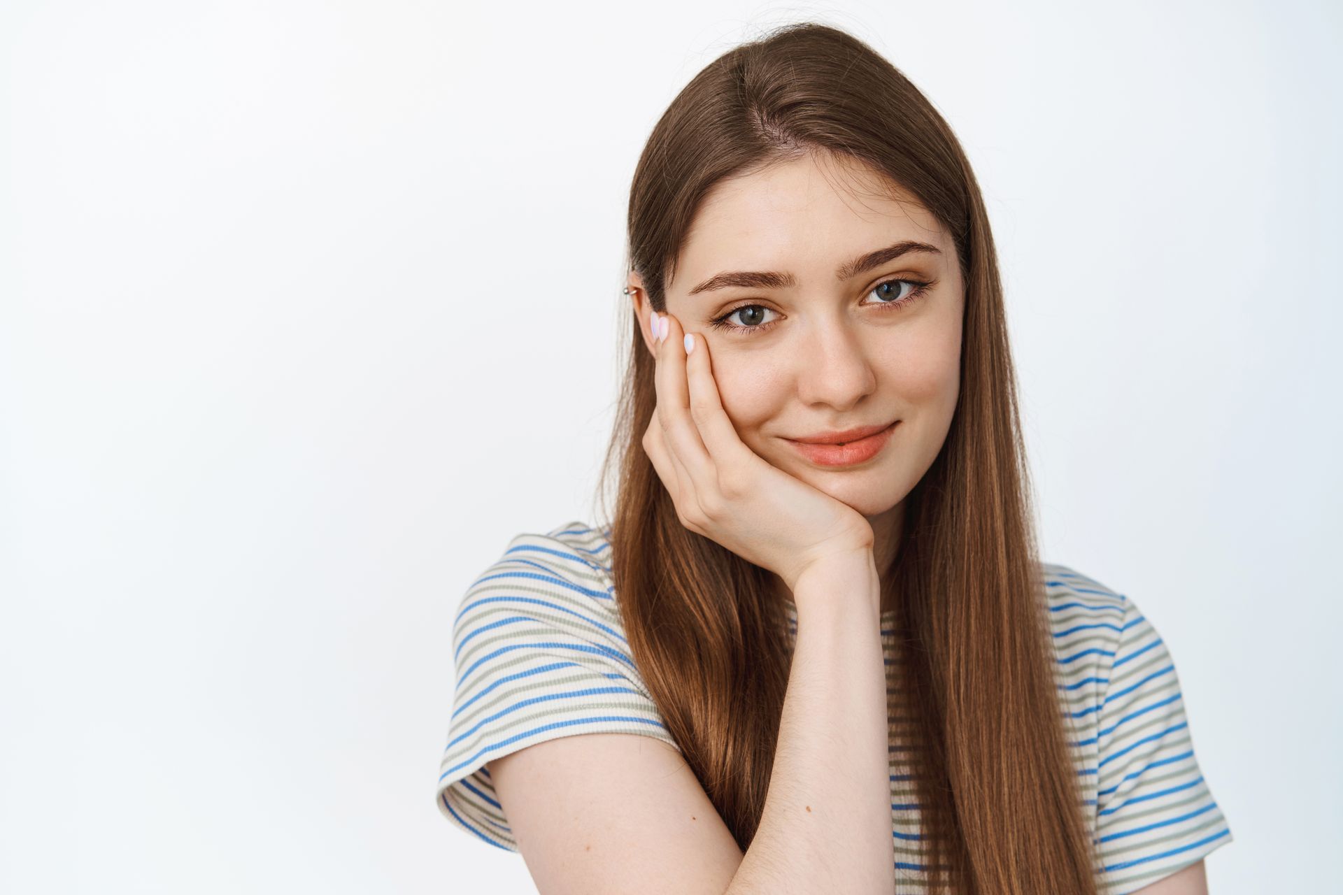 A young woman is holding her hand to her face and smiling.