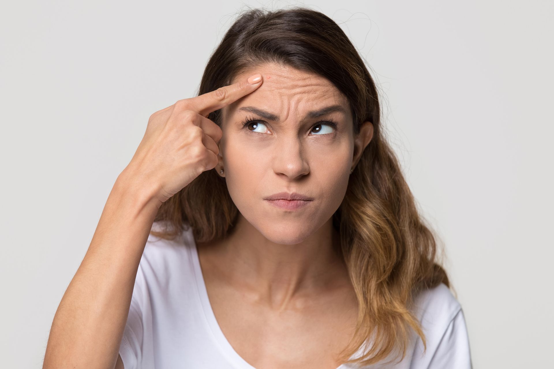 A woman is scratching her forehead with her finger.