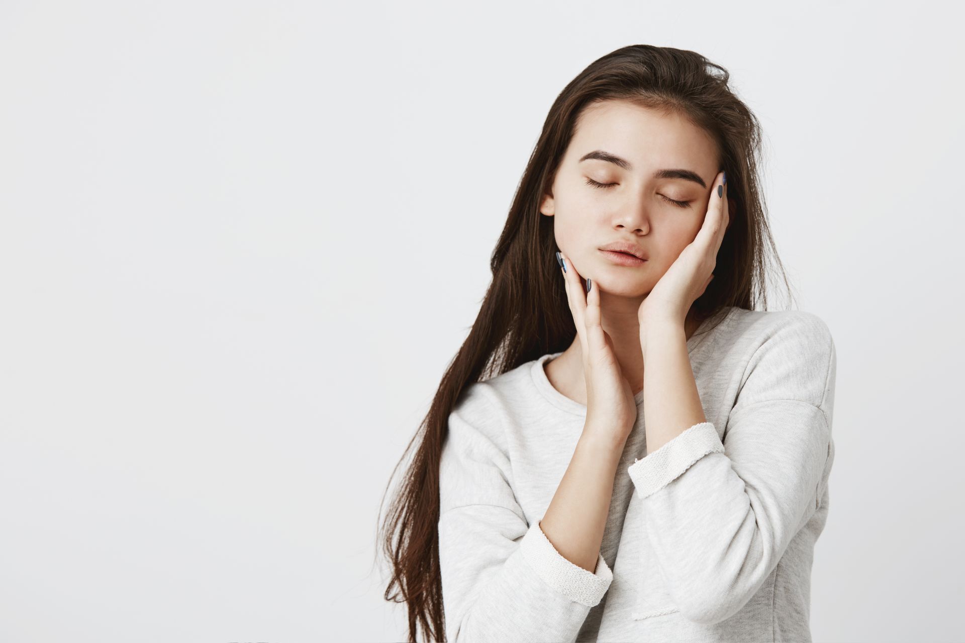 A woman in a white sweater is covering her face with her hands.