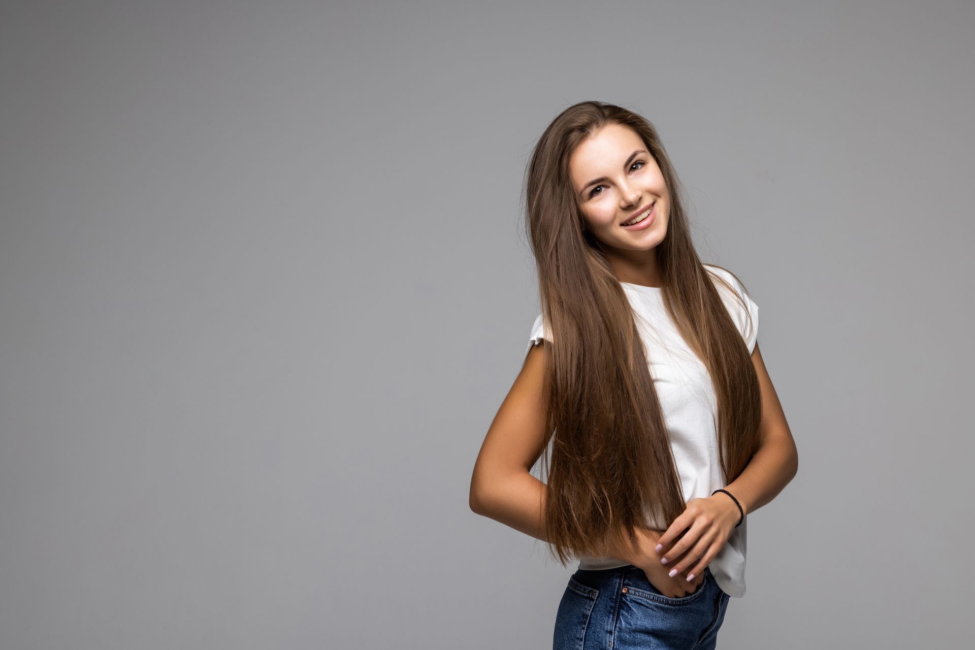 A woman with long hair is standing in front of a gray background and smiling.