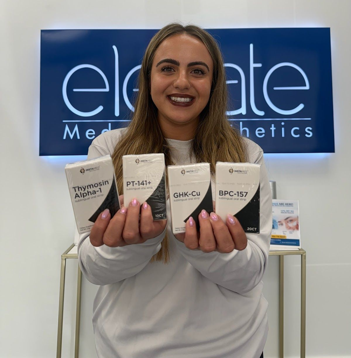 A woman in a white shirt is smiling with her arms crossed and her hand on her chin.