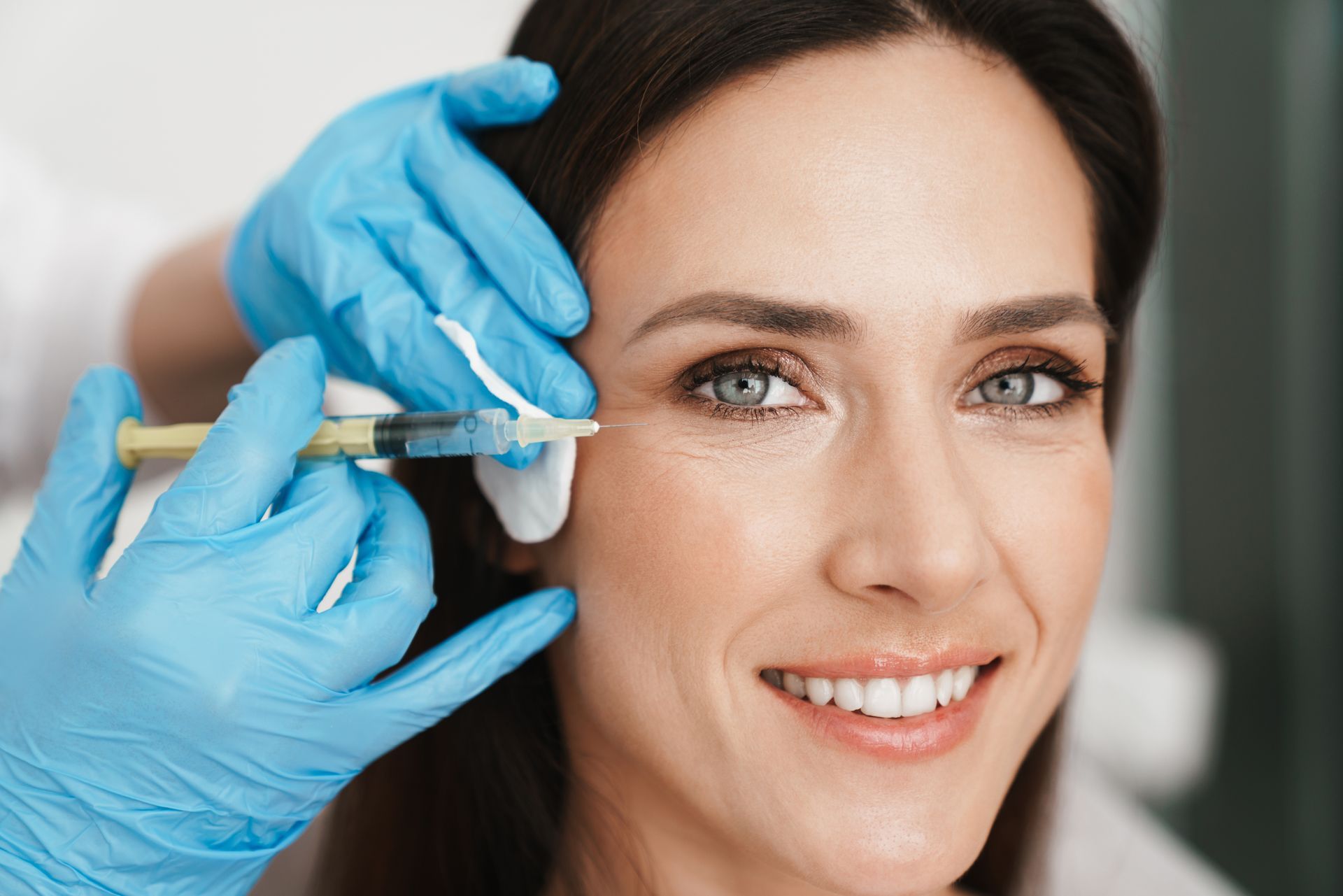 Woman receiving an injection near her eye, blue gloves, smiling, indoors.