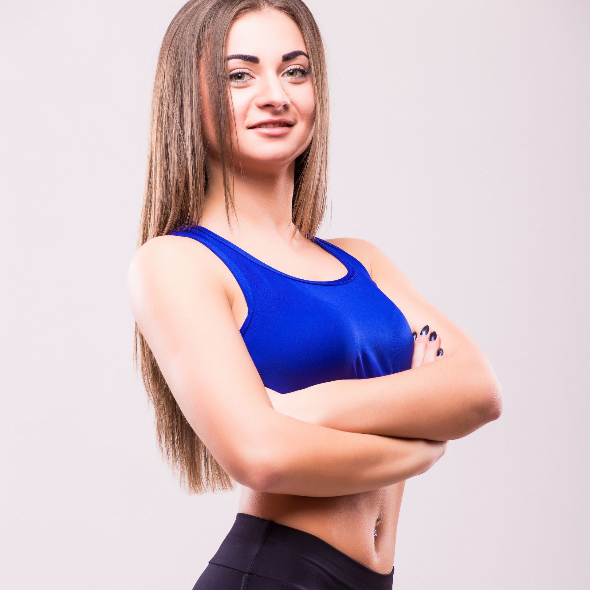 A woman in a blue sports bra is standing with her arms crossed.