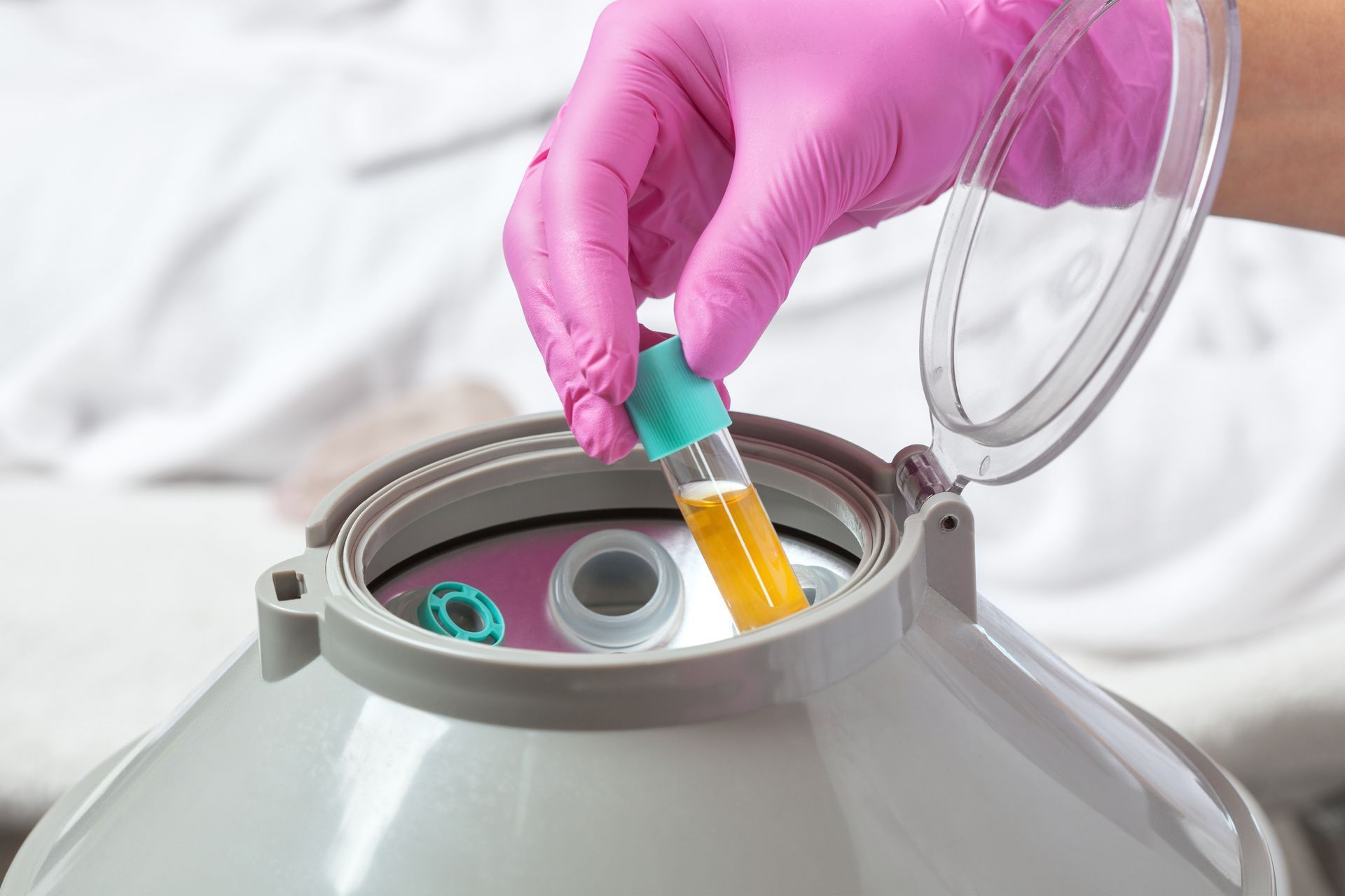 A person wearing pink gloves is holding a test tube with a yellow liquid in it.
