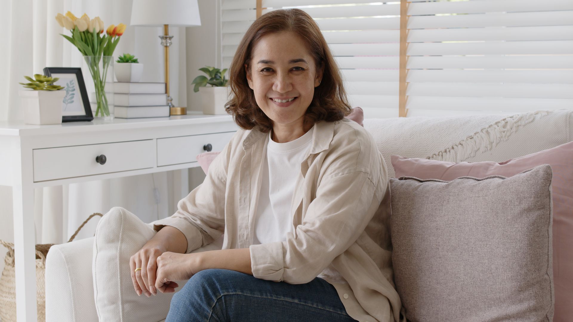 A woman in a white sweater is sitting in front of a window.