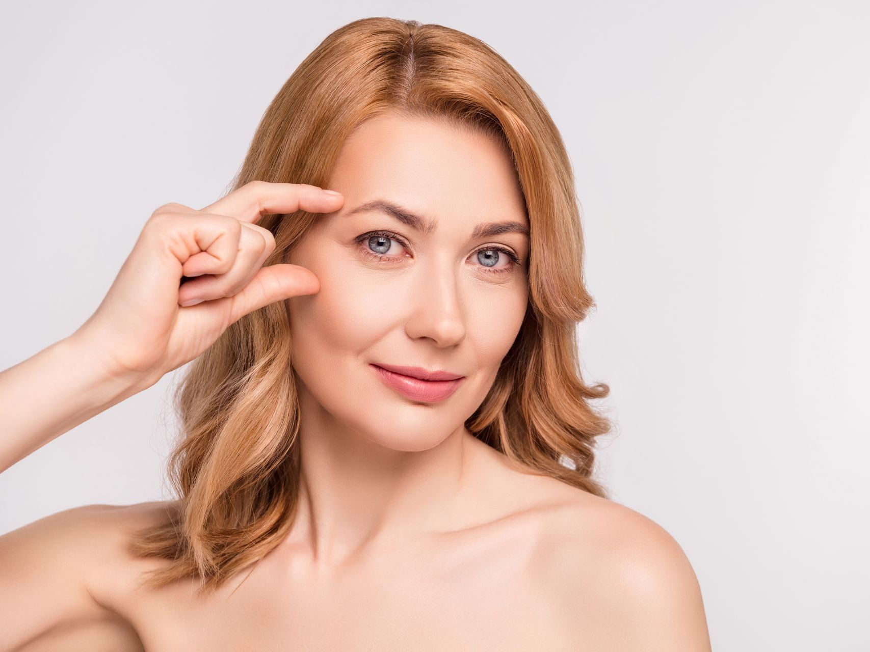 A woman is pointing at her eyebrow with her finger.