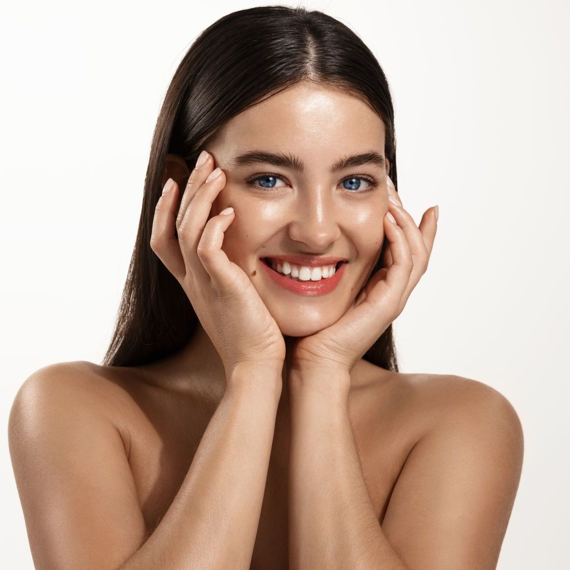 A woman is smiling with her hands on her face.