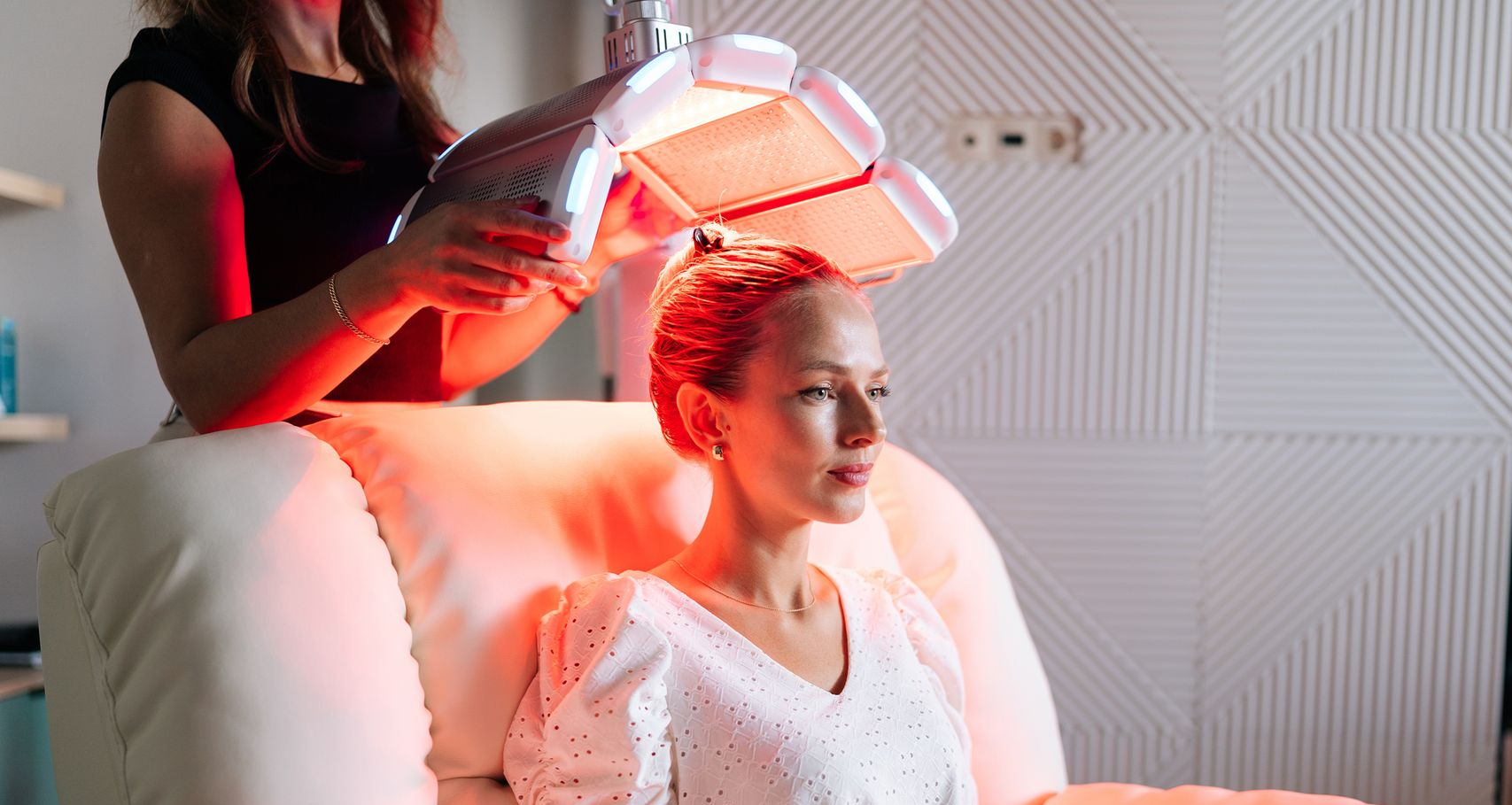 A woman with long hair is standing in front of a gray background and smiling.