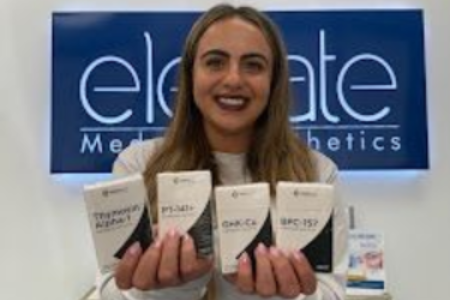A woman in a white shirt is smiling with her arms crossed and her hand on her chin.