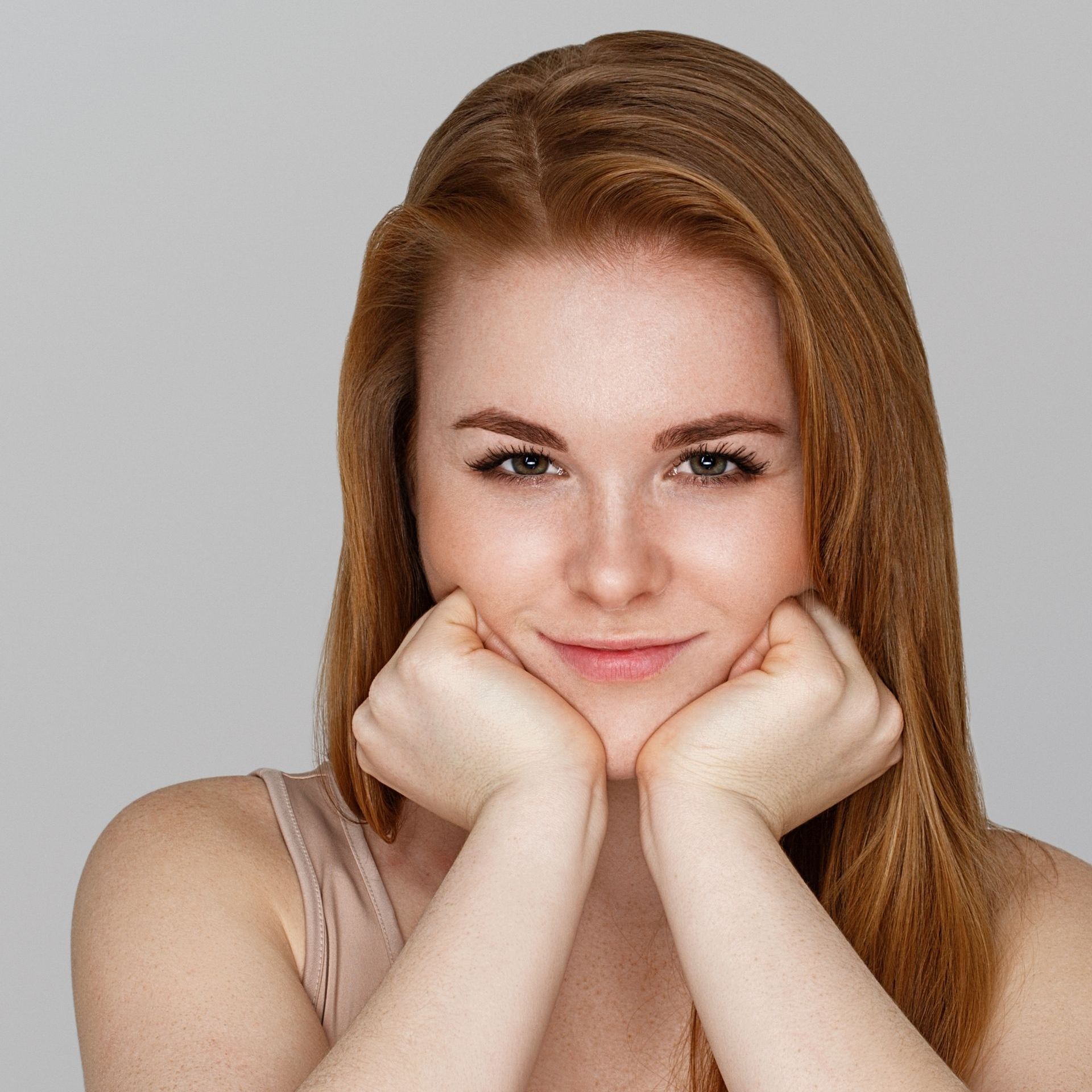A woman with red hair is smiling with her hands on her face.