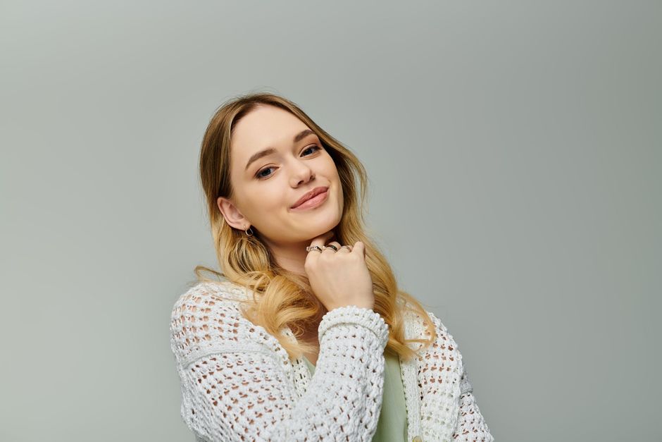A woman in a white sweater is smiling and holding her hand to her chin.