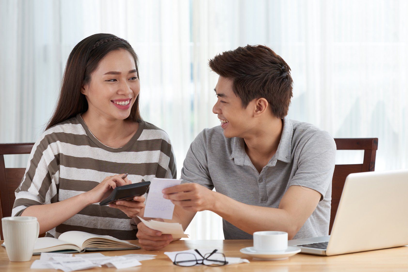 A man and a woman are sitting at a table with a laptop and a calculator.
