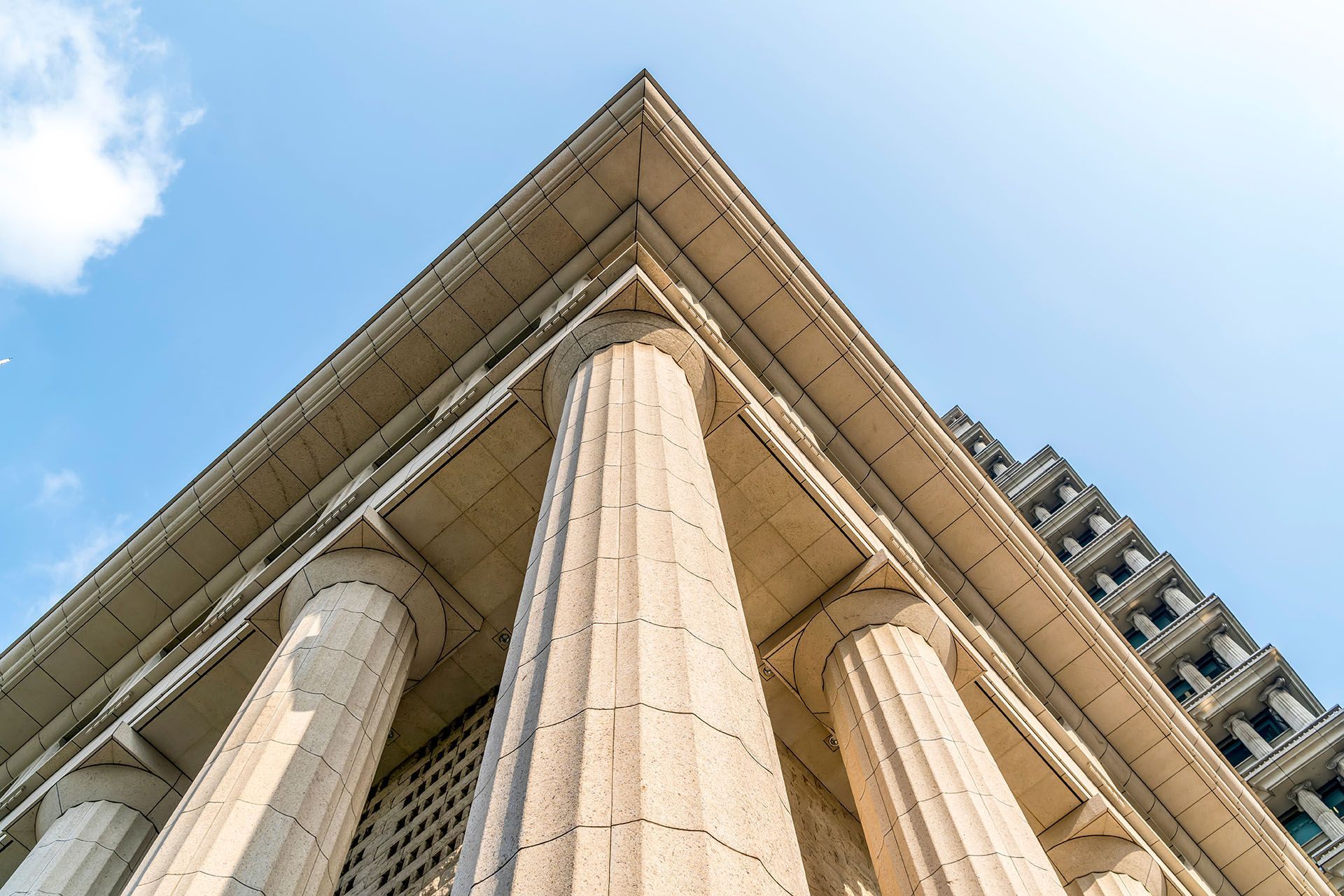 Looking up at the top of a building with columns against a blue sky.