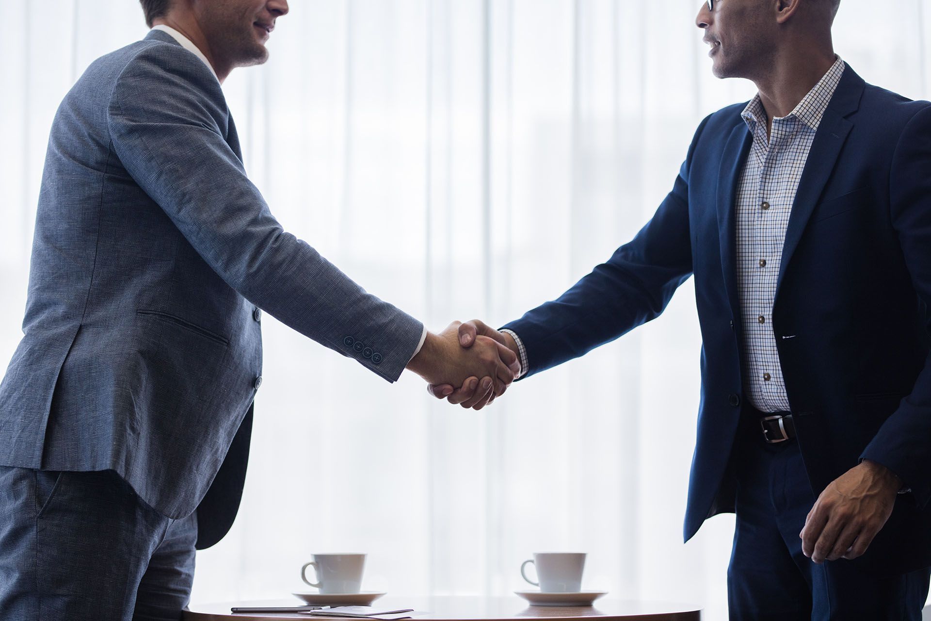 two men are shaking hands over a table with cups of coffee