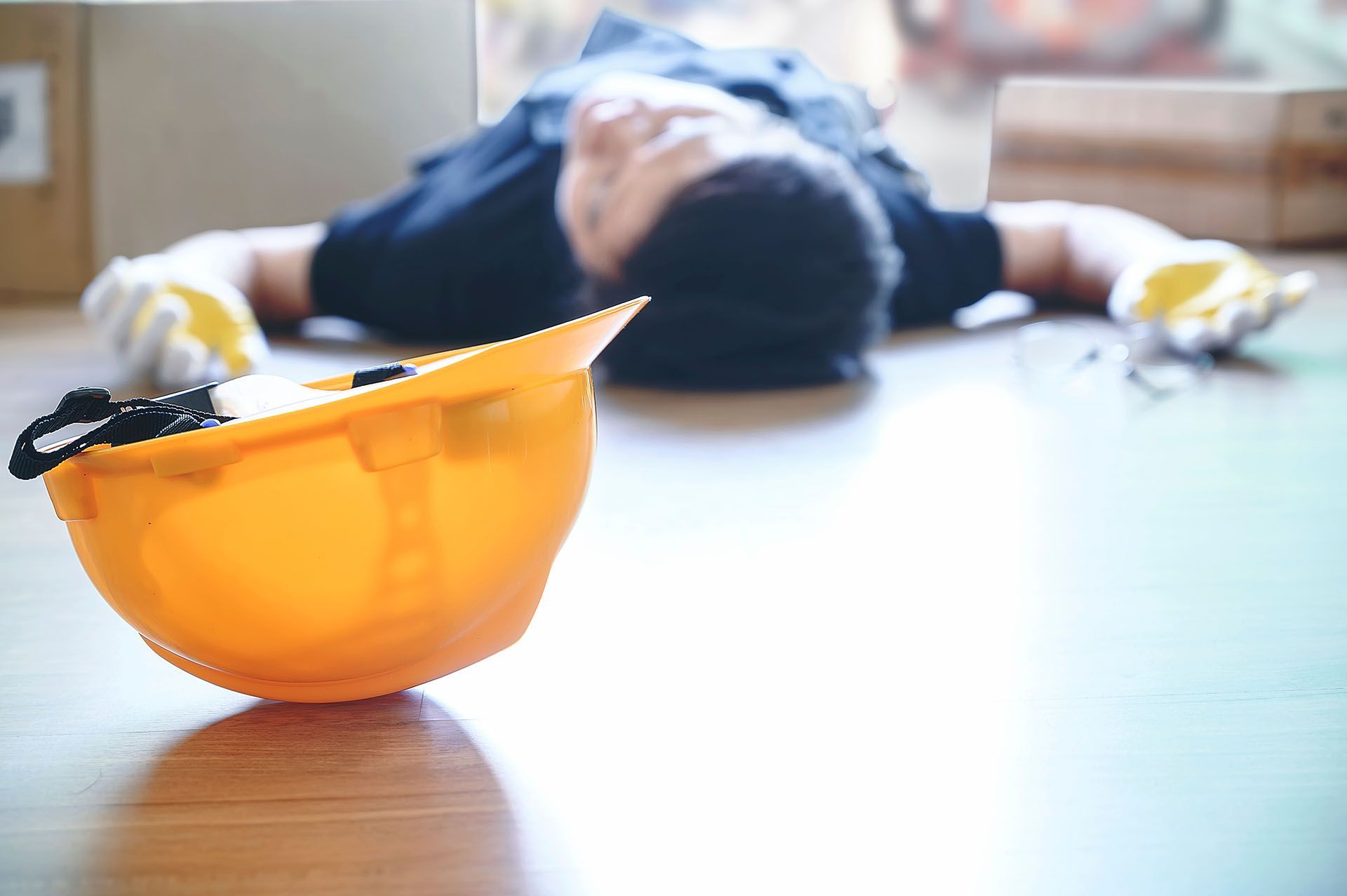A man is laying on the floor next to a hard hat.