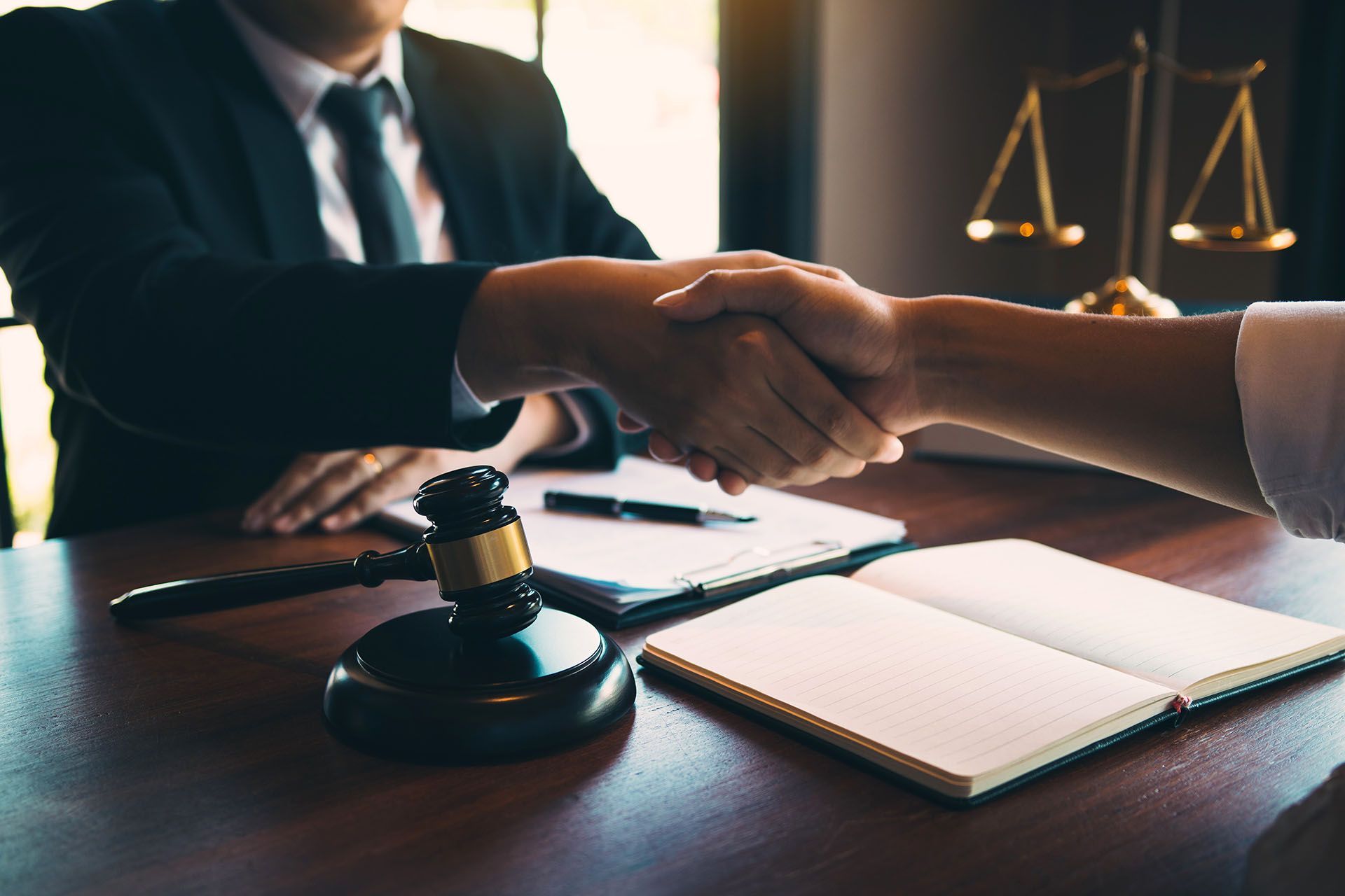 A judge is shaking hands with a client in front of a scale of justice.
