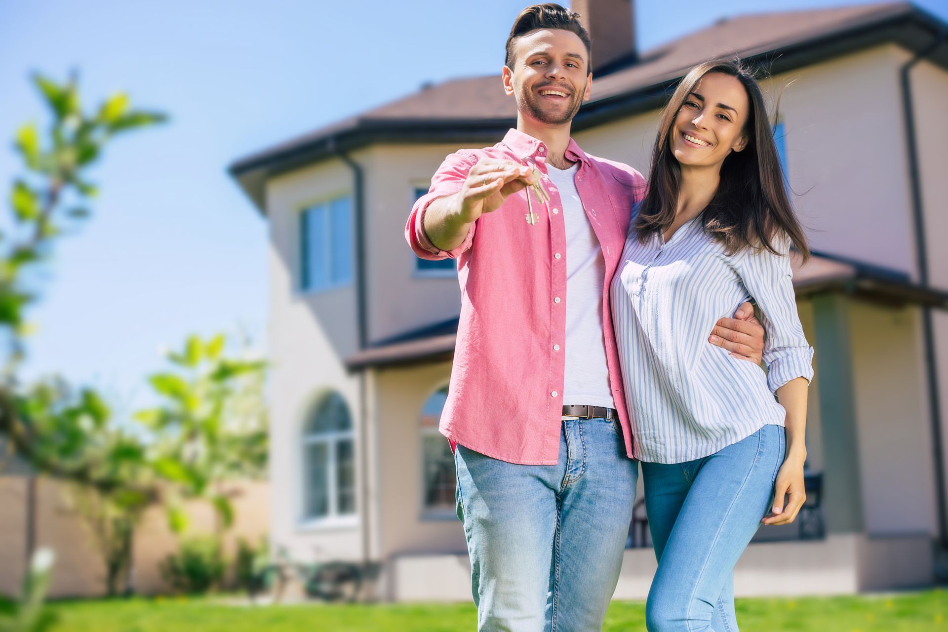 A man and a woman are standing in front of a house holding keys.