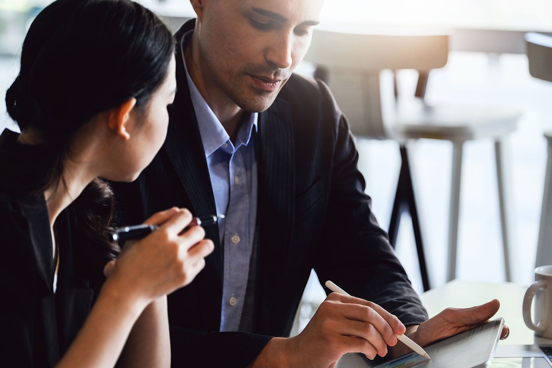 A man and a woman are sitting at a table looking at a tablet.