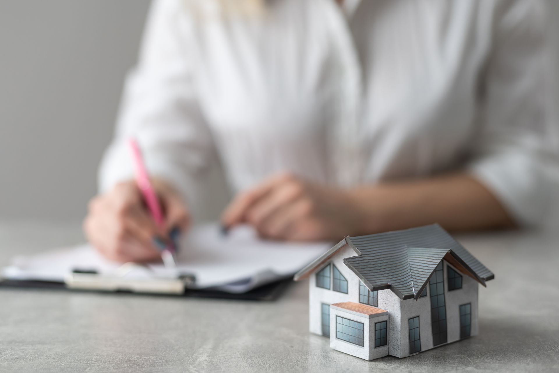 A woman is writing on a clipboard next to a model house.