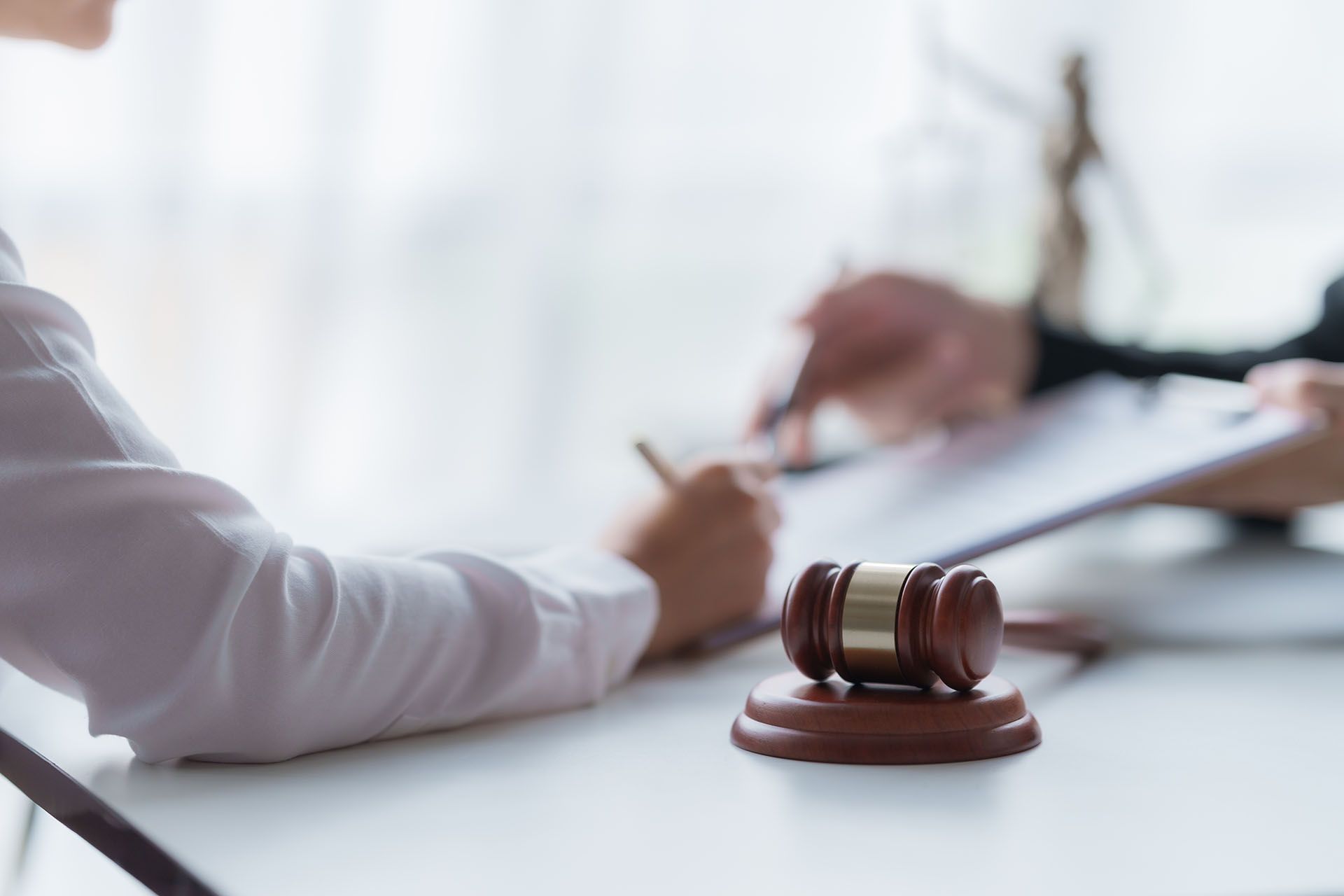 A judge's gavel is sitting on a table next to a person signing a document.