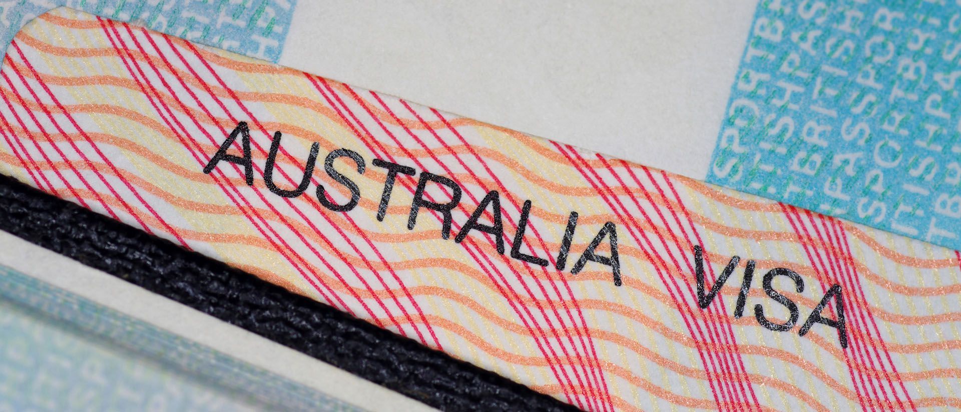 Australia Visa, close-up. Text on a patterned beige/red surface, over a dark edge and a pale blue background with lettering.