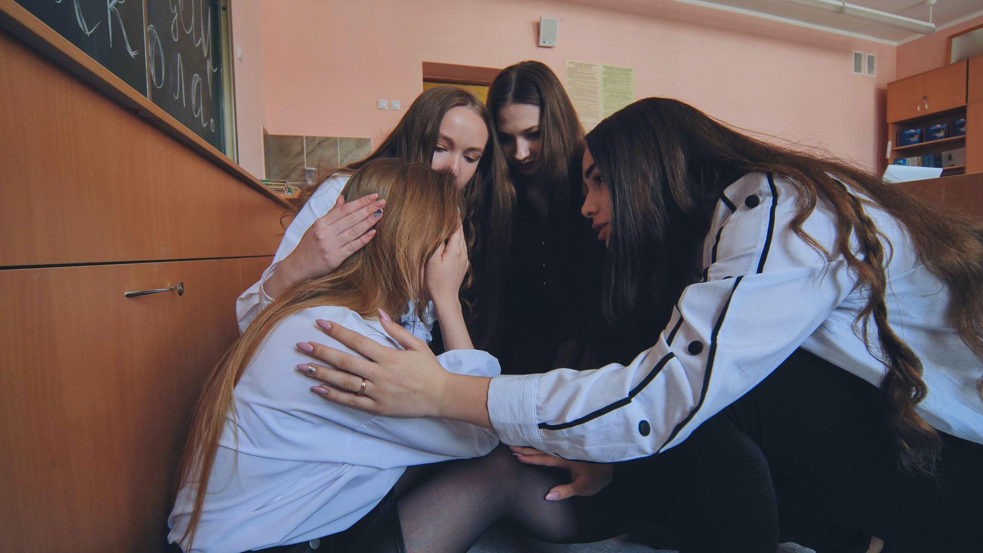 A group of girls are hugging each other in a classroom.