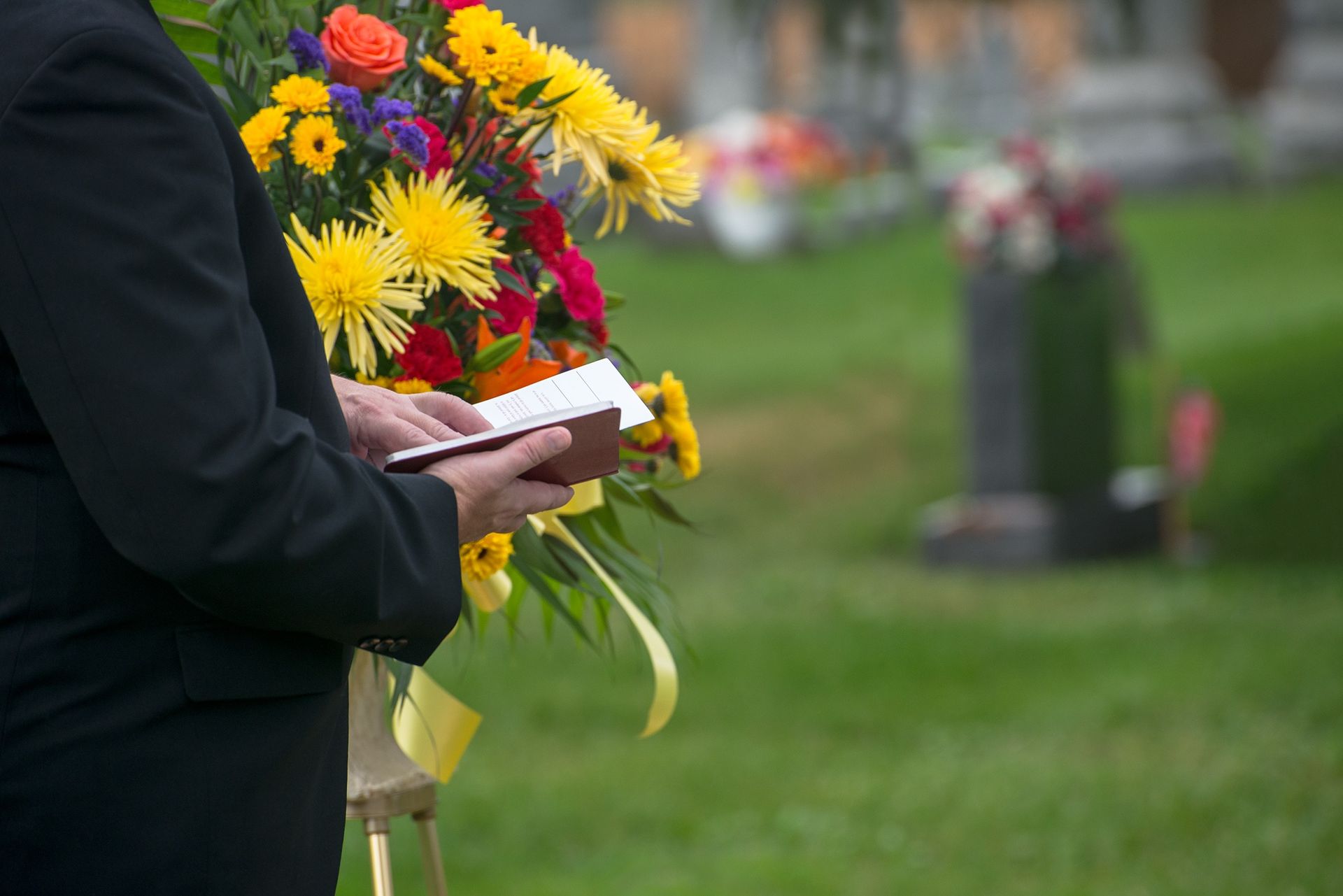 A man is holding a bible and a bouquet of flowers in a cemetery.