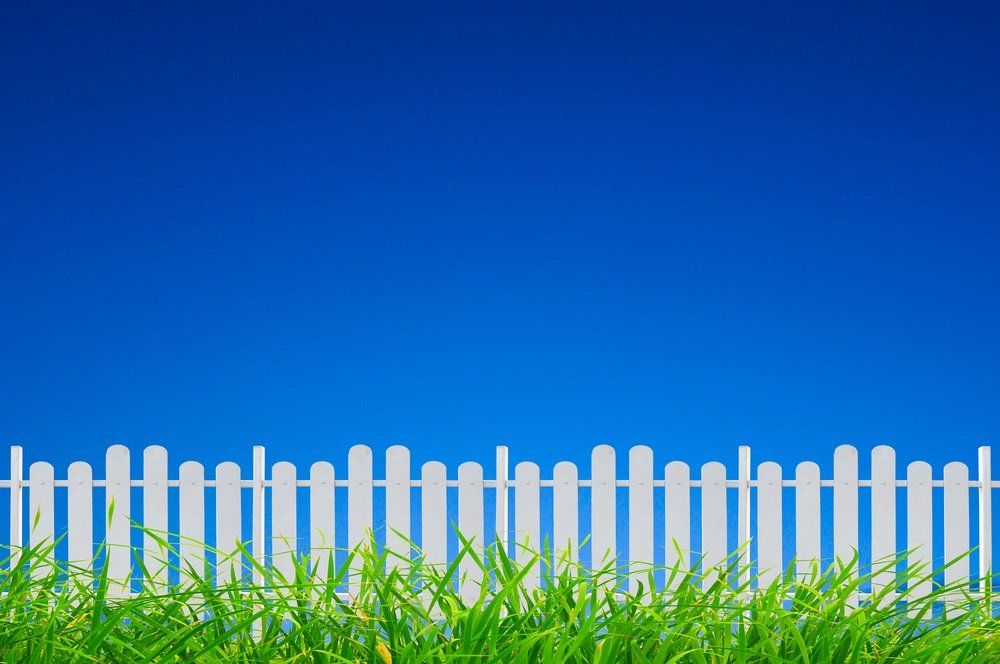 a white picket fence is surrounded by green grass against a blue sky