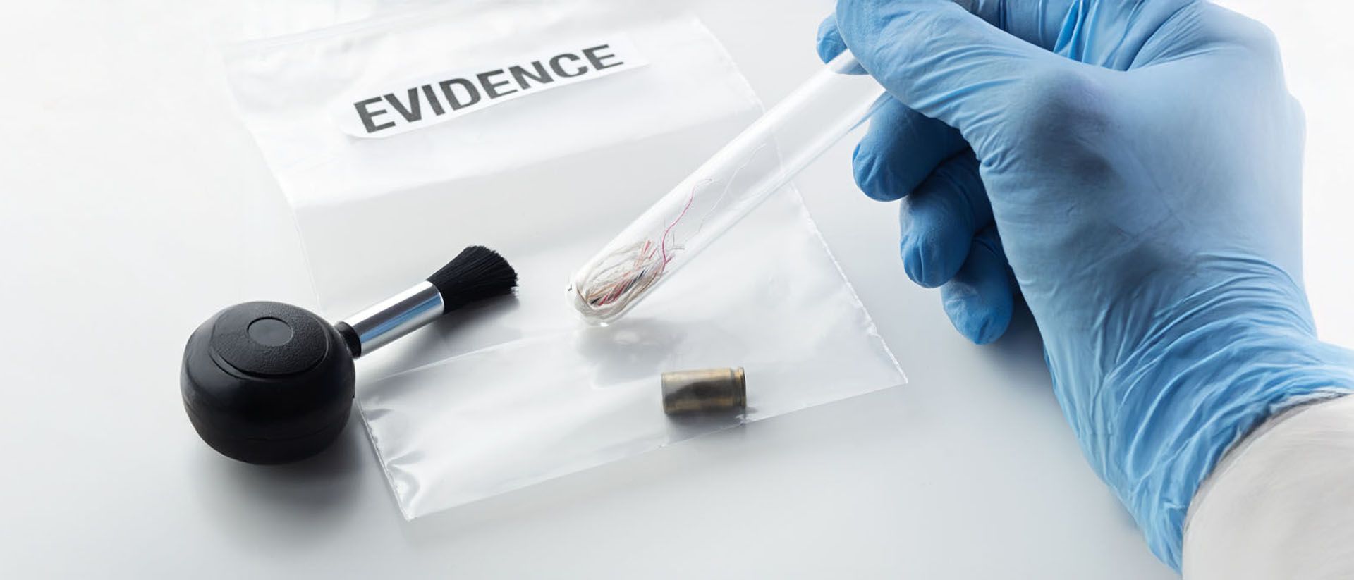 A gloved hand holding a test tube over evidence bags with the word 