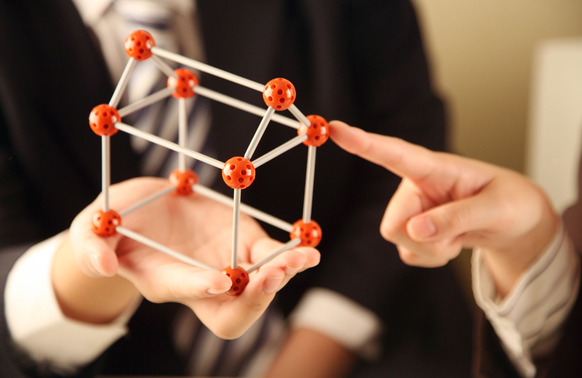 A man in a suit and tie is pointing at a model of a cube