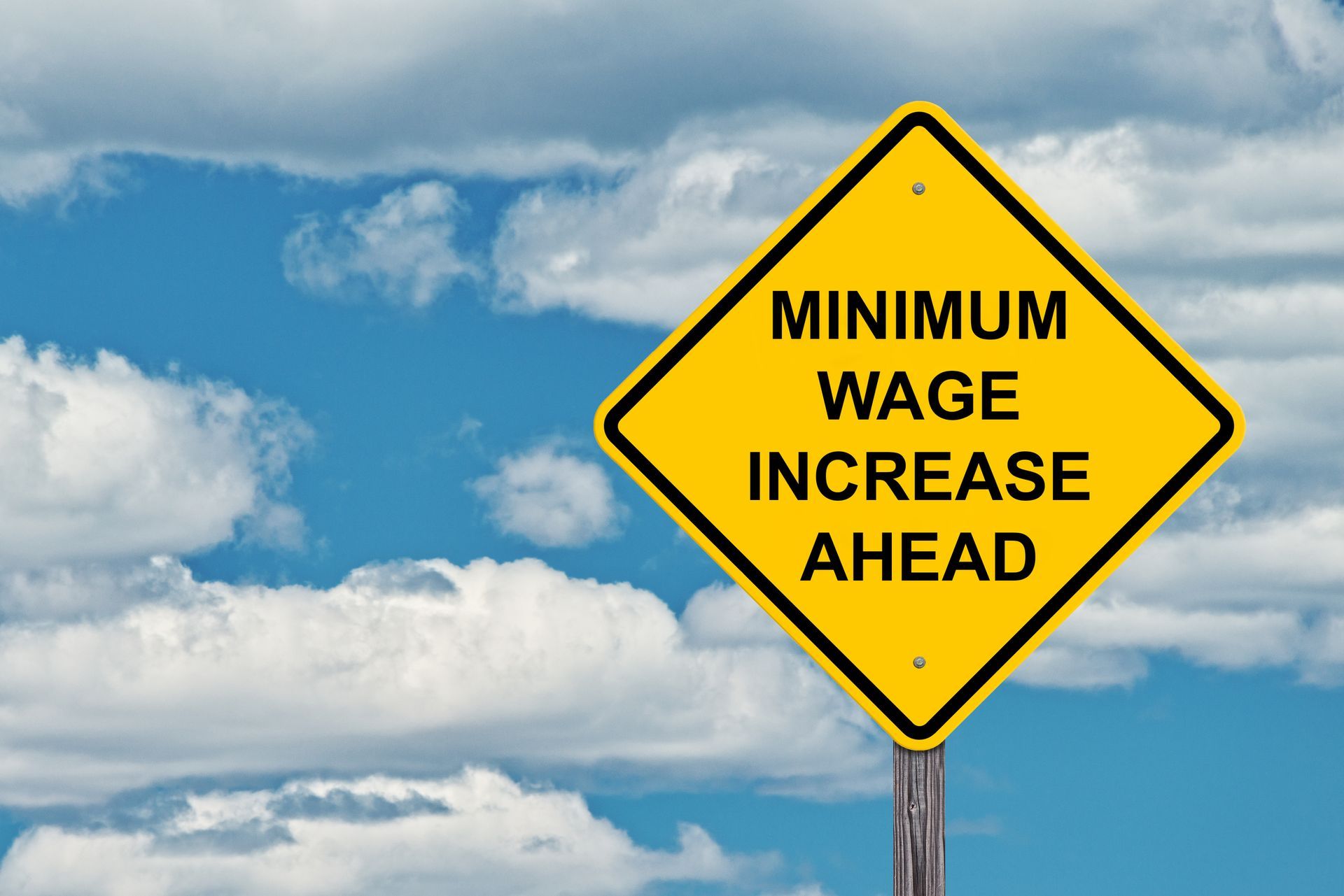A yellow sign that says minimum wage increase ahead
