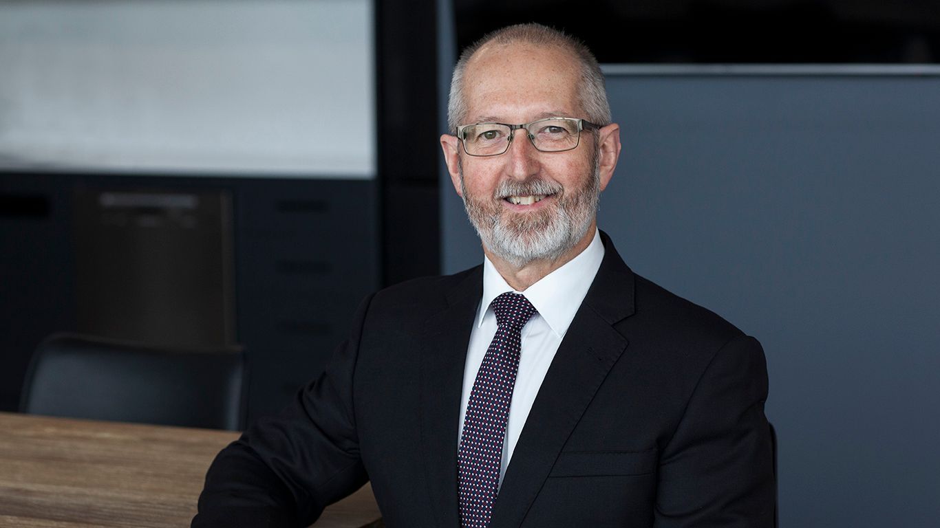 Man in suit and tie, smiling, indoors.