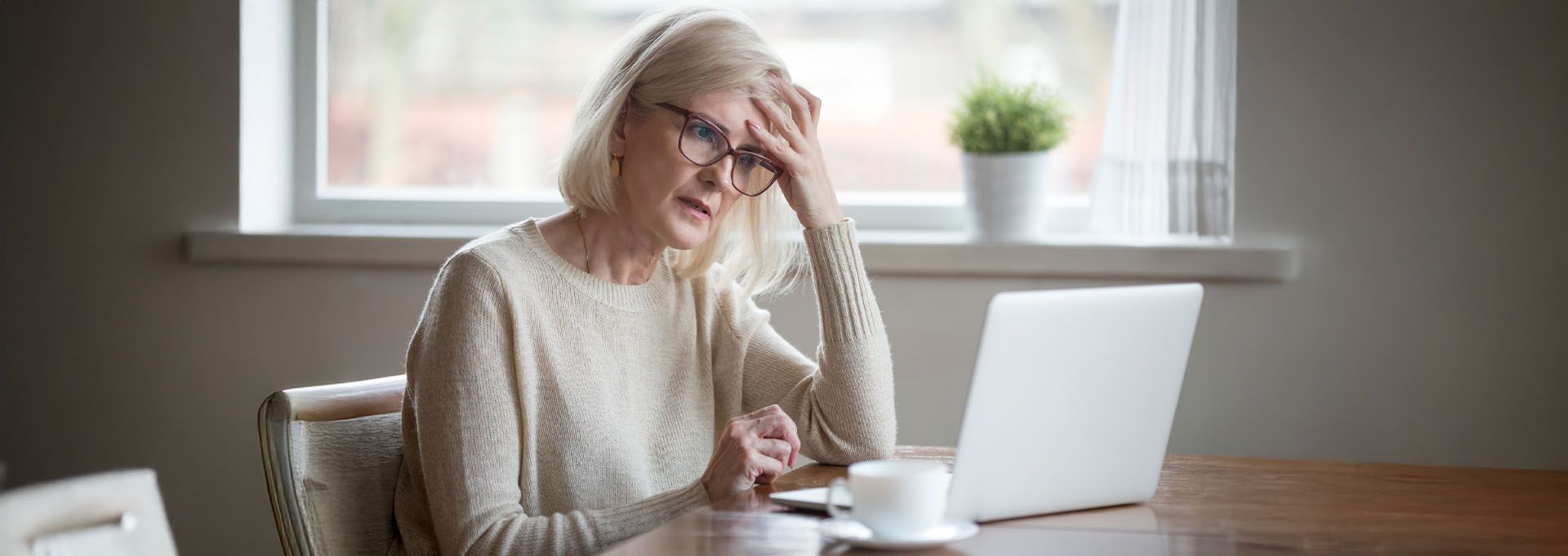 An older woman is sitting at a table using a laptop computer.