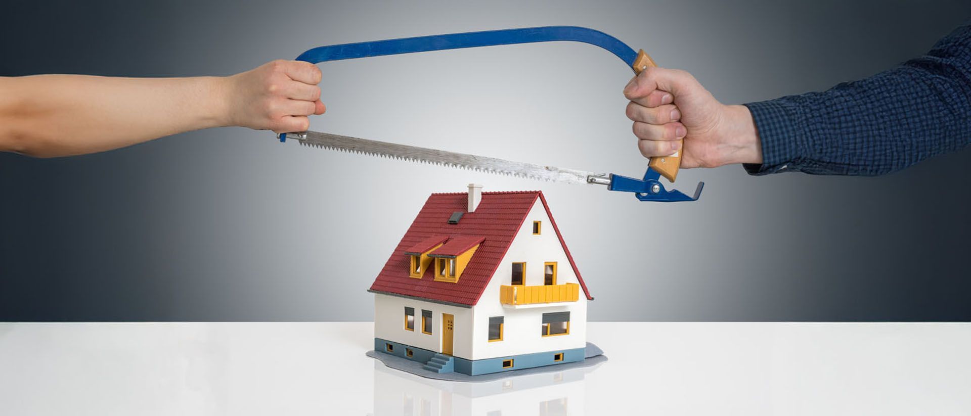 Two hands sawing a model house in half; divorce, separation concept.